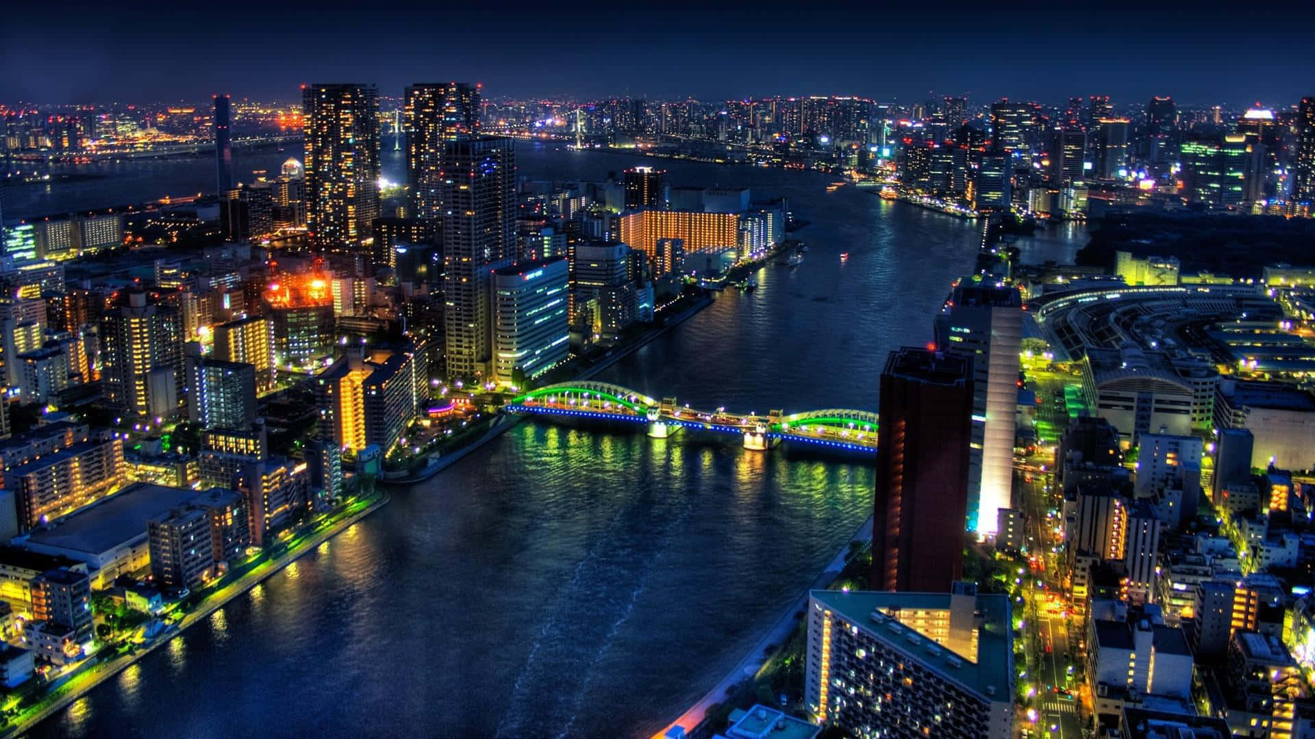 bridge 桌布 壁紙 — 充滿活力的城市景觀鳥瞰夜景，閃爍的摩天大樓和橫跨黑暗河流的彩色橋樑。
