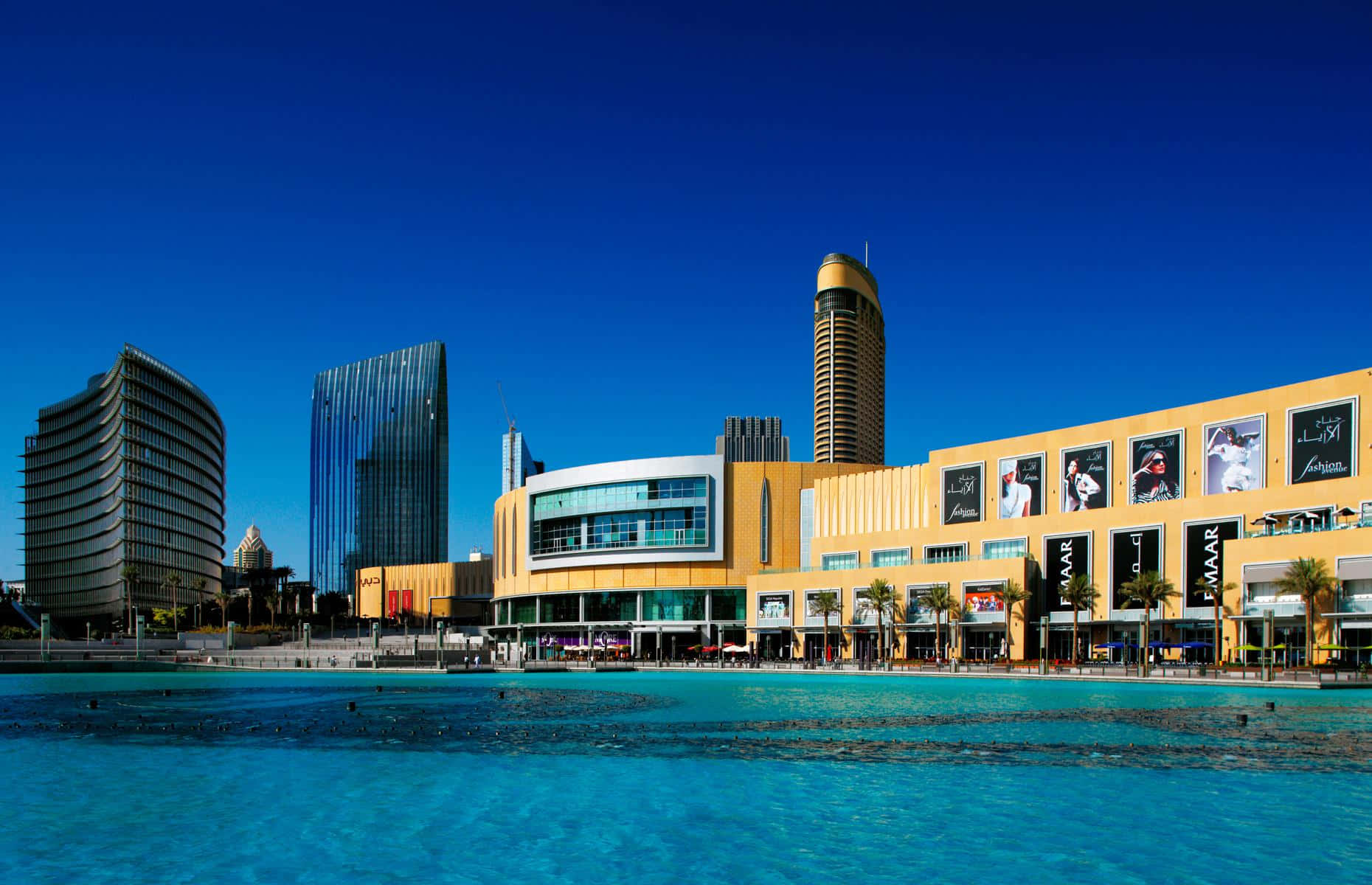 Mall 桌布 壁紙 — 充滿活力的城市海濱場景，現代玻璃和金色建築在清澈藍天下倒映在碧綠的水中。