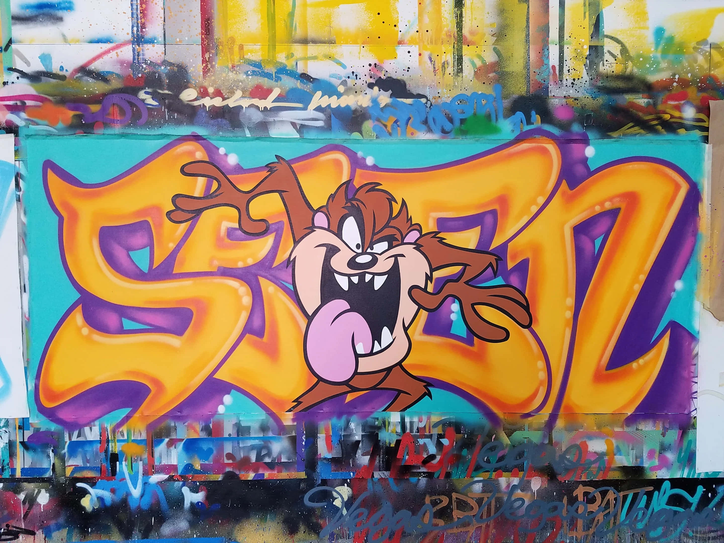 Graffiti Art 桌布 壁紙 — 充滿活力的塗鴉壁畫，描繪塔斯馬尼亞惡魔塔茲從大膽的橙色和紫色風格化字母中爆發出來，背景是混亂的城市景觀。