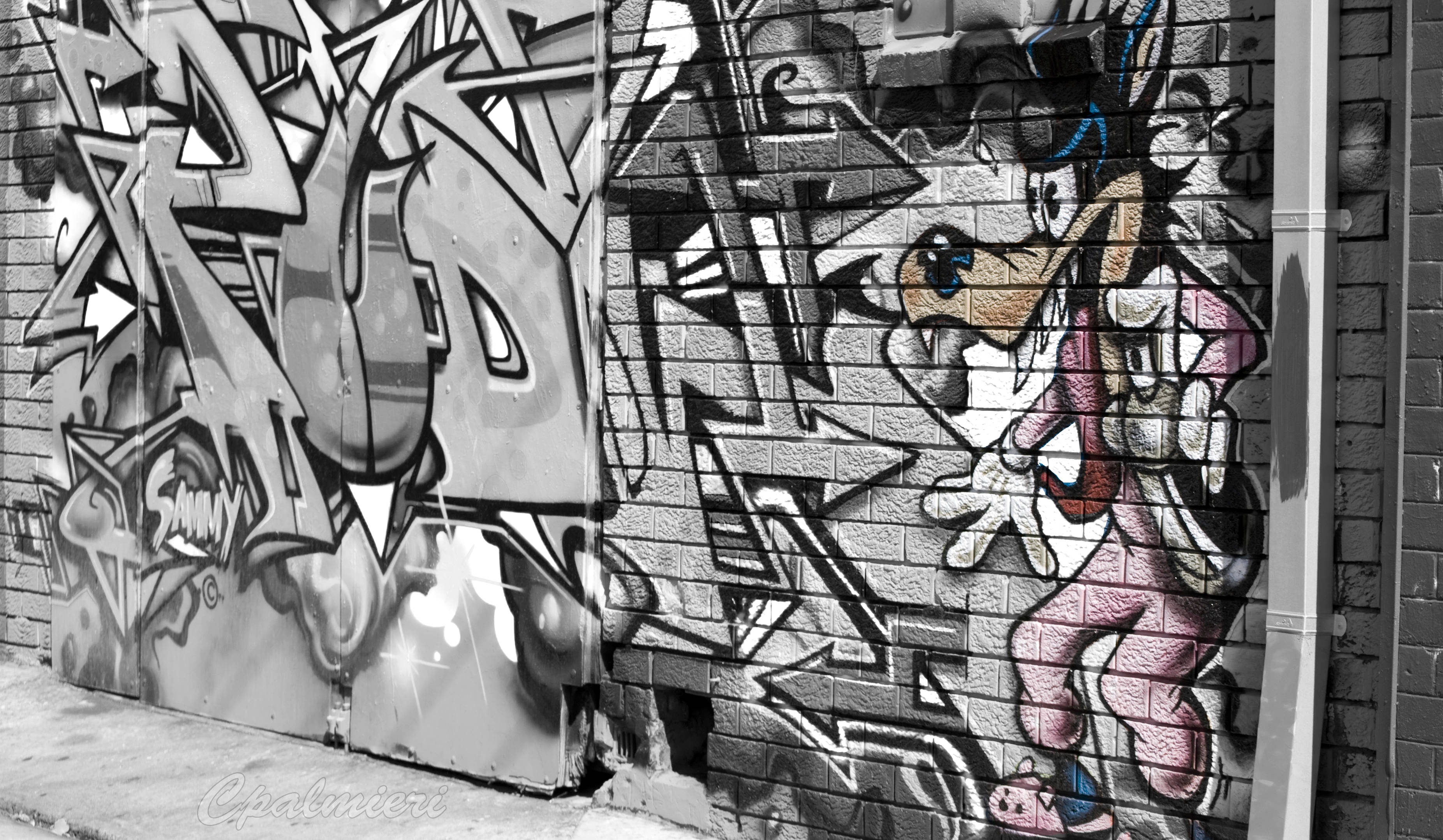 Black And White Graffiti 桌布 壁紙 — 充滿活力的塗鴉藝術，以卡通角色和粗體字覆蓋城市小巷中風化的磚牆。