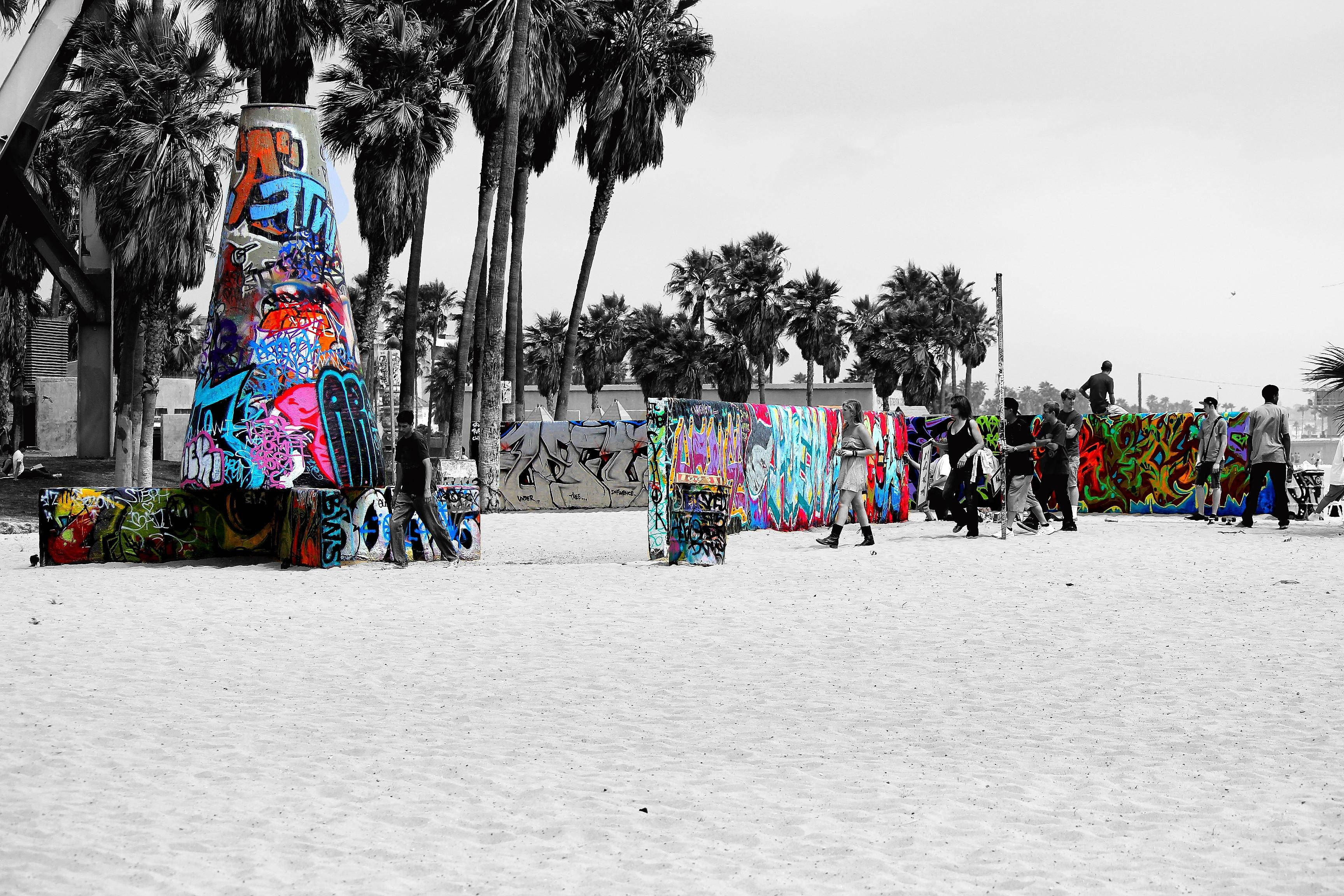 Venice Beach 桌布 壁紙 — 充滿活力的塗鴉覆蓋結構在黑白背景下，在沙灘上與棕櫚樹和人羣形成鮮明對比。