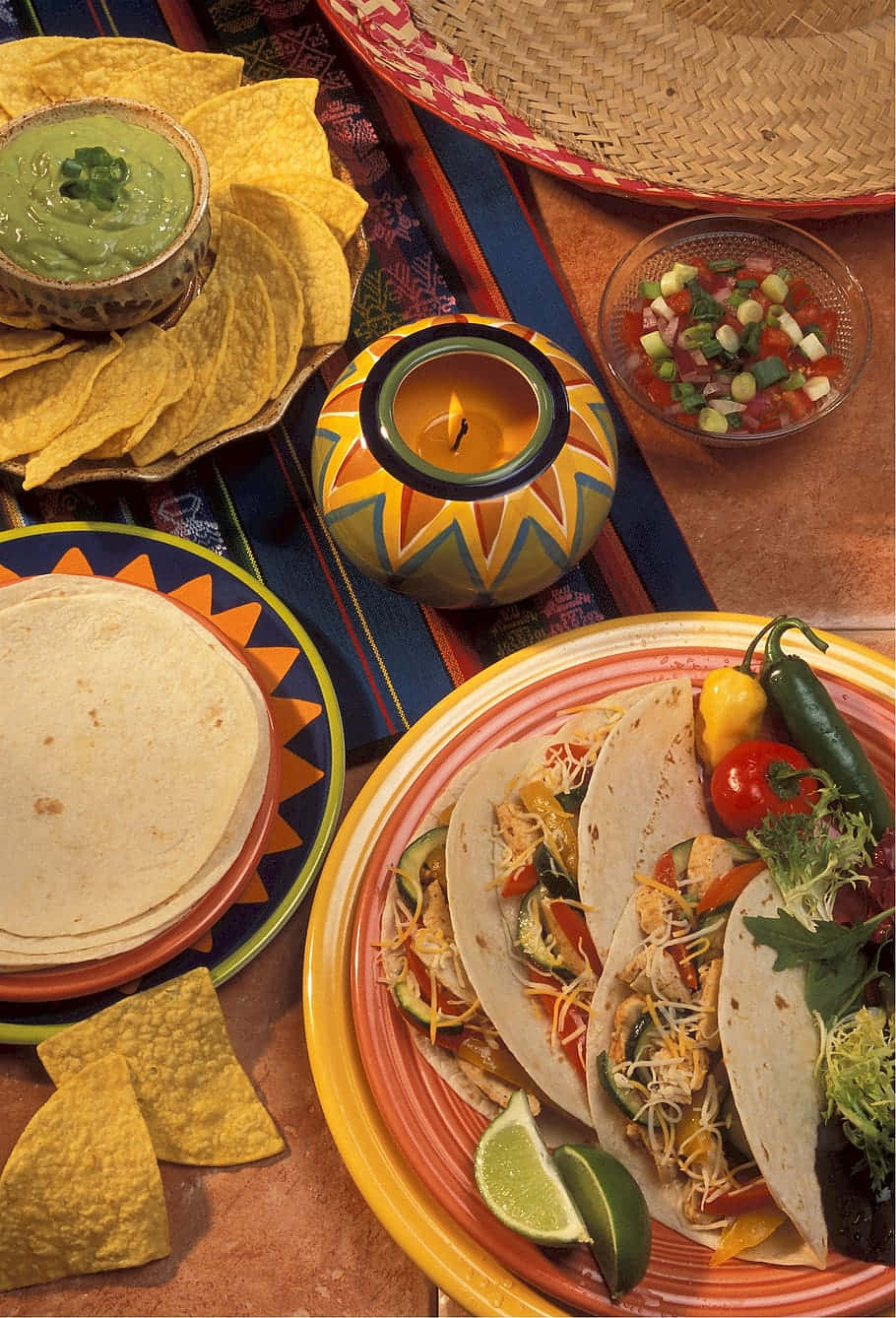 Mexican 桌布 壁紙 — 充滿活力的墨西哥餐，色彩繽紛的塔可、酪梨醬、莎莎醬和玉米餅放在有圖案的盤子上，並點燃一支蠟燭。
