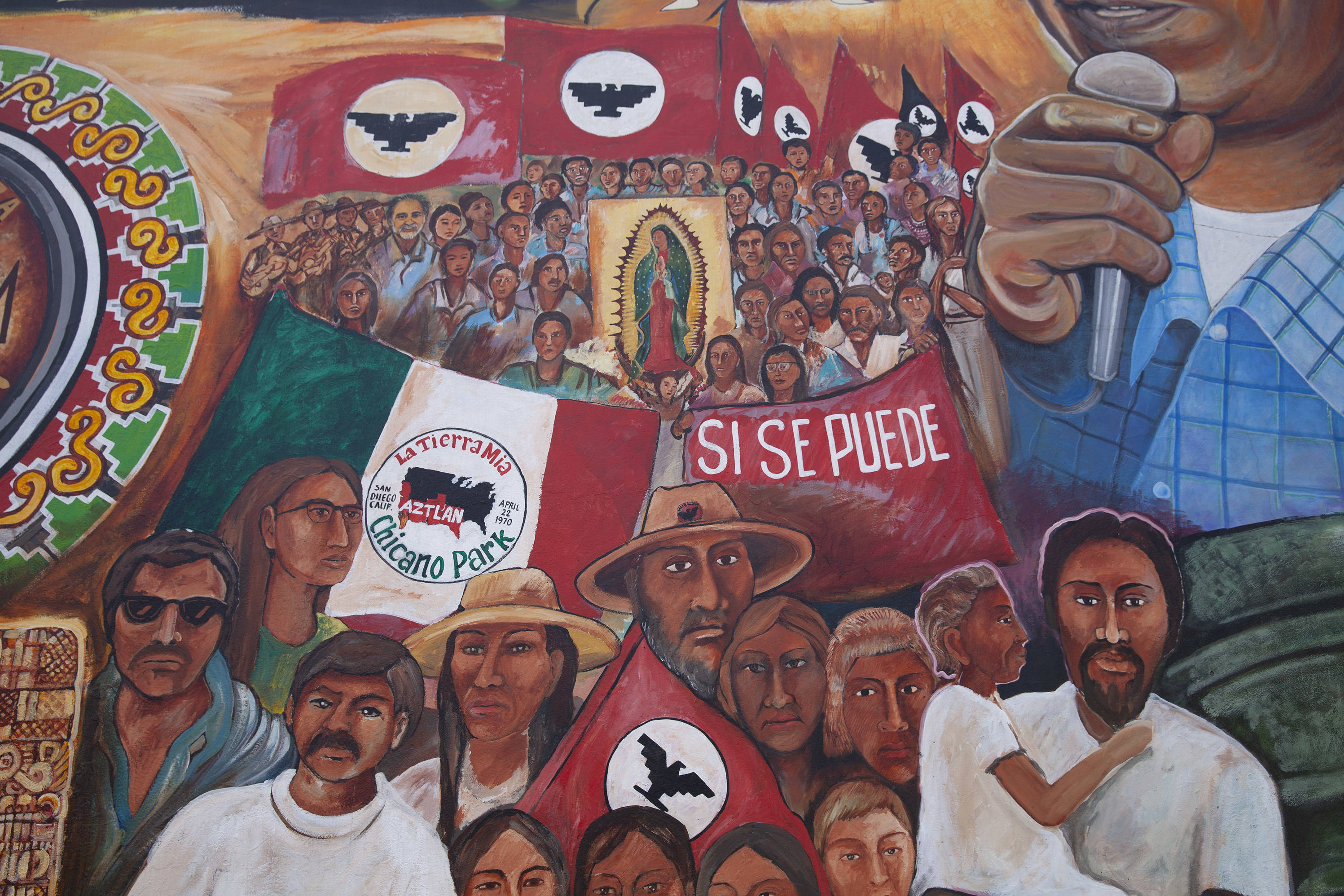 Chicano 桌布 壁紙 — 充滿活力的壁畫，描繪了多元社區人物在彩繪天空下手持旗幟和「Si Se Puede」橫幅。