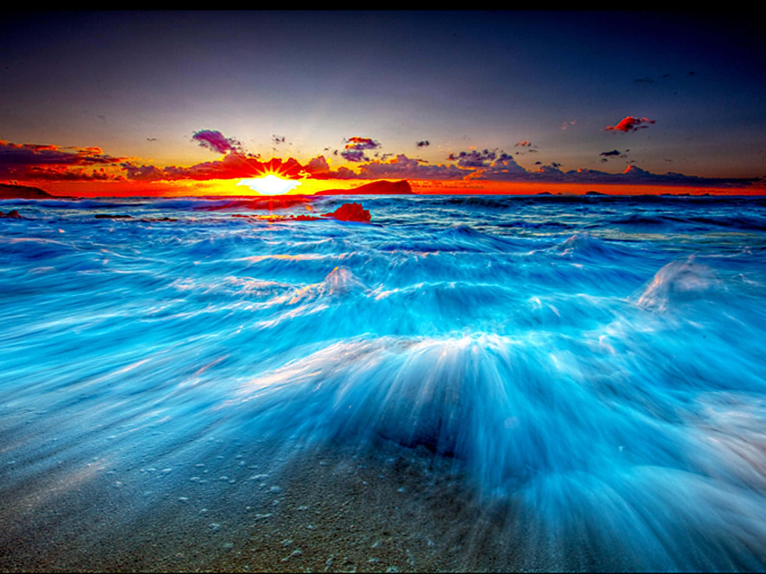3d Ocean 桌布 壁紙 — 充滿活力的夕陽將天空染成火熱的橙色和紫色，翠綠色的海浪奔騰向岸邊。