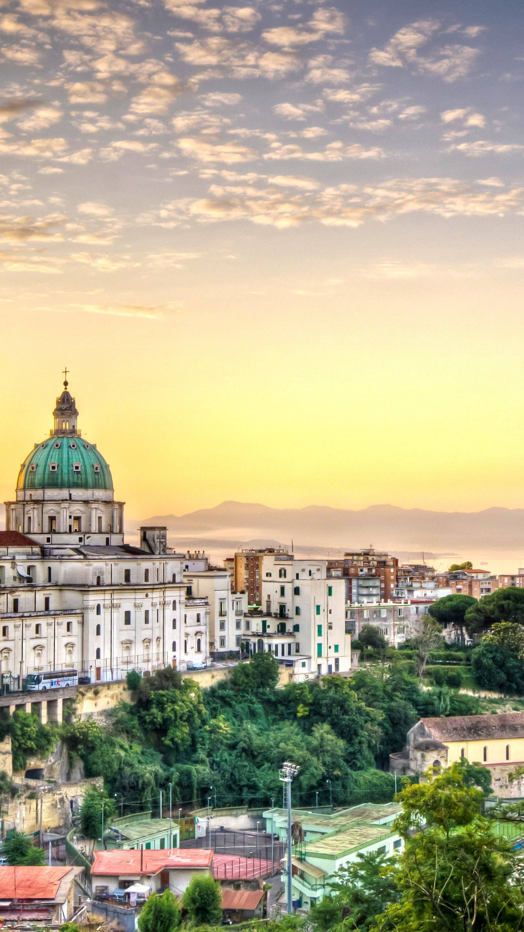 Naples 桌布 壁紙 — 充滿活力的夕陽沐浴著山坡城市景觀，其中有一座突出的綠色圓頂大教堂和陶土屋頂。