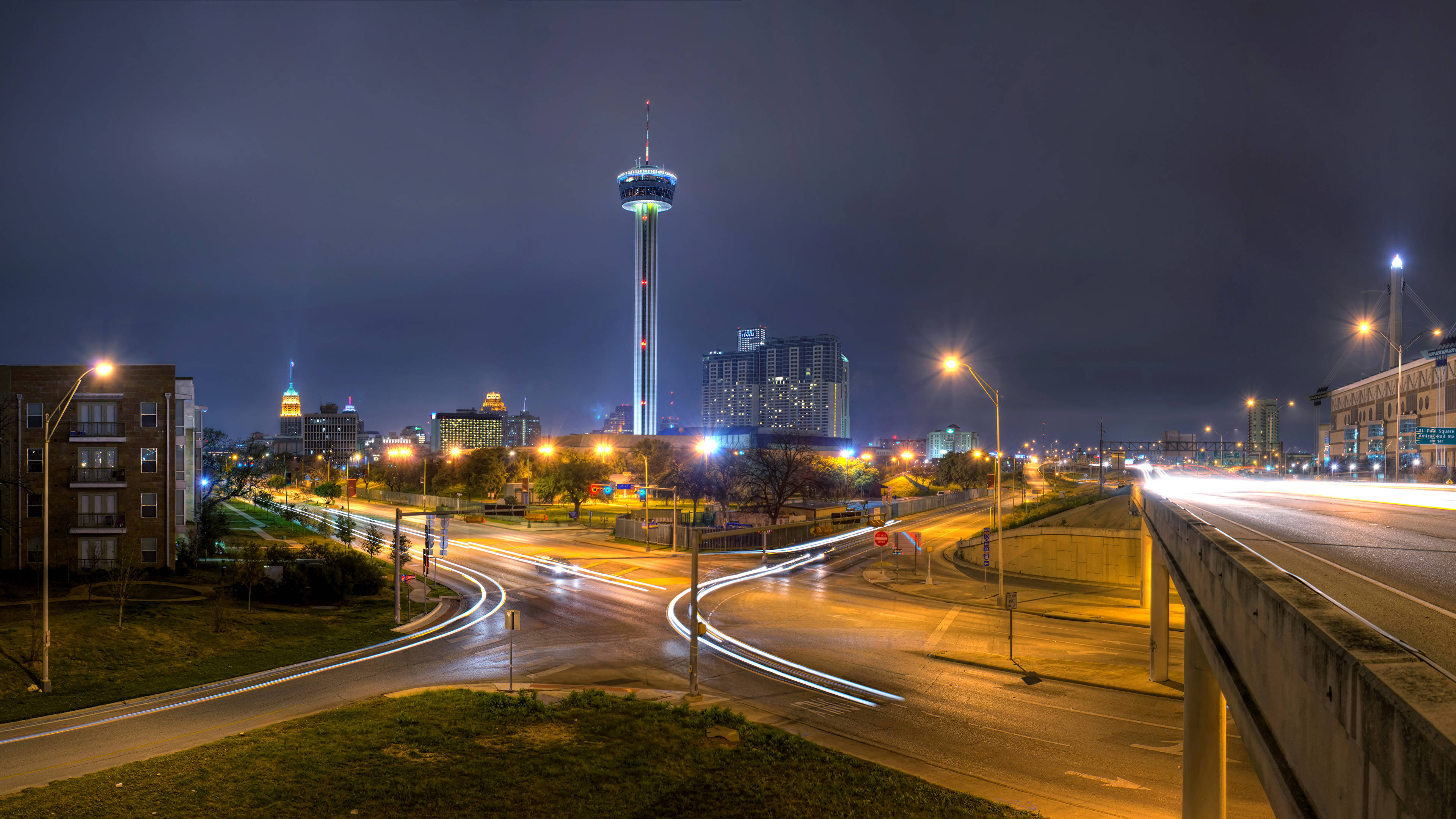 城市 桌布 壁紙 — 充滿活力的夜景，以發光的塔樓和濕滑道路上的汽車燈光軌跡為特色。