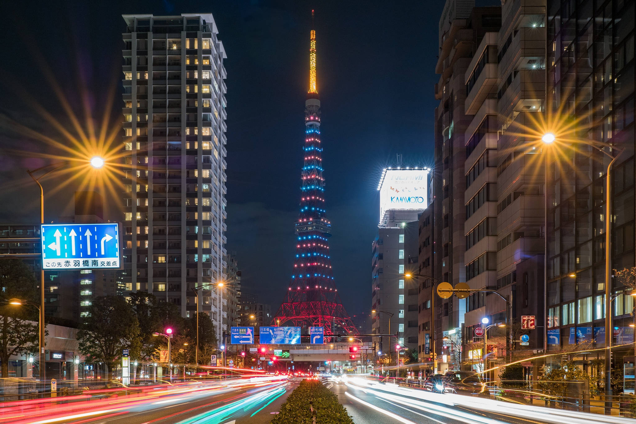 日本 桌布 壁紙 — 充滿活力的夜景，東京塔閃爍著紅、藍、黃光，被高樓大廈和汽車燈光軌跡環繞。