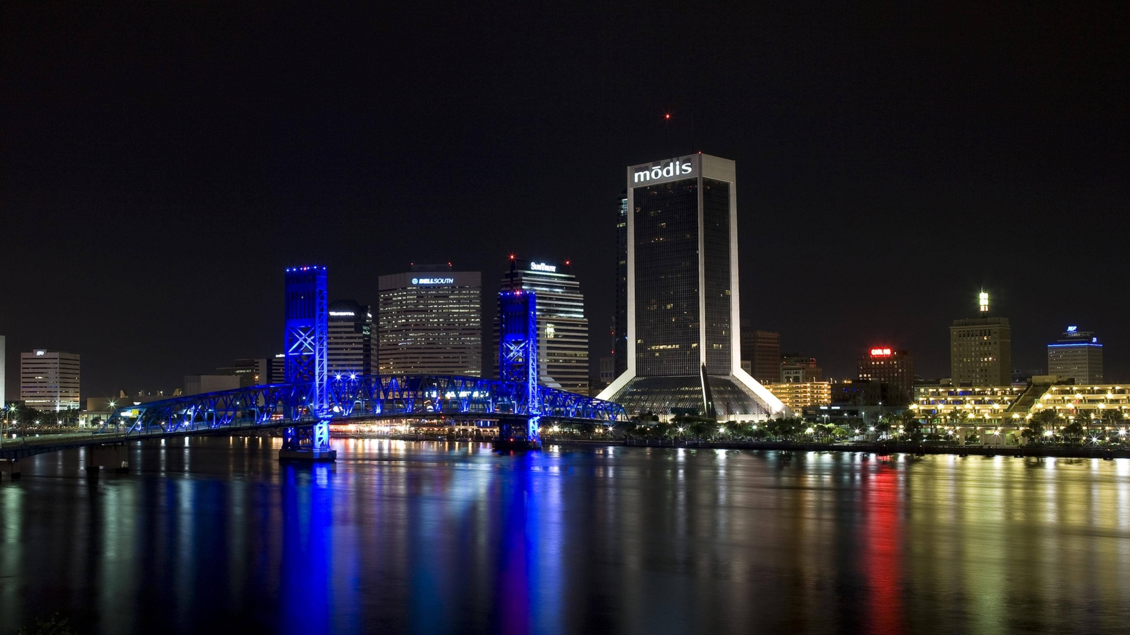 Jacksonville 桌布 壁紙 — 充滿活力的夜景，特色是水面上發光的藍色橋樑，摩天大樓倒映在平靜的河流中。