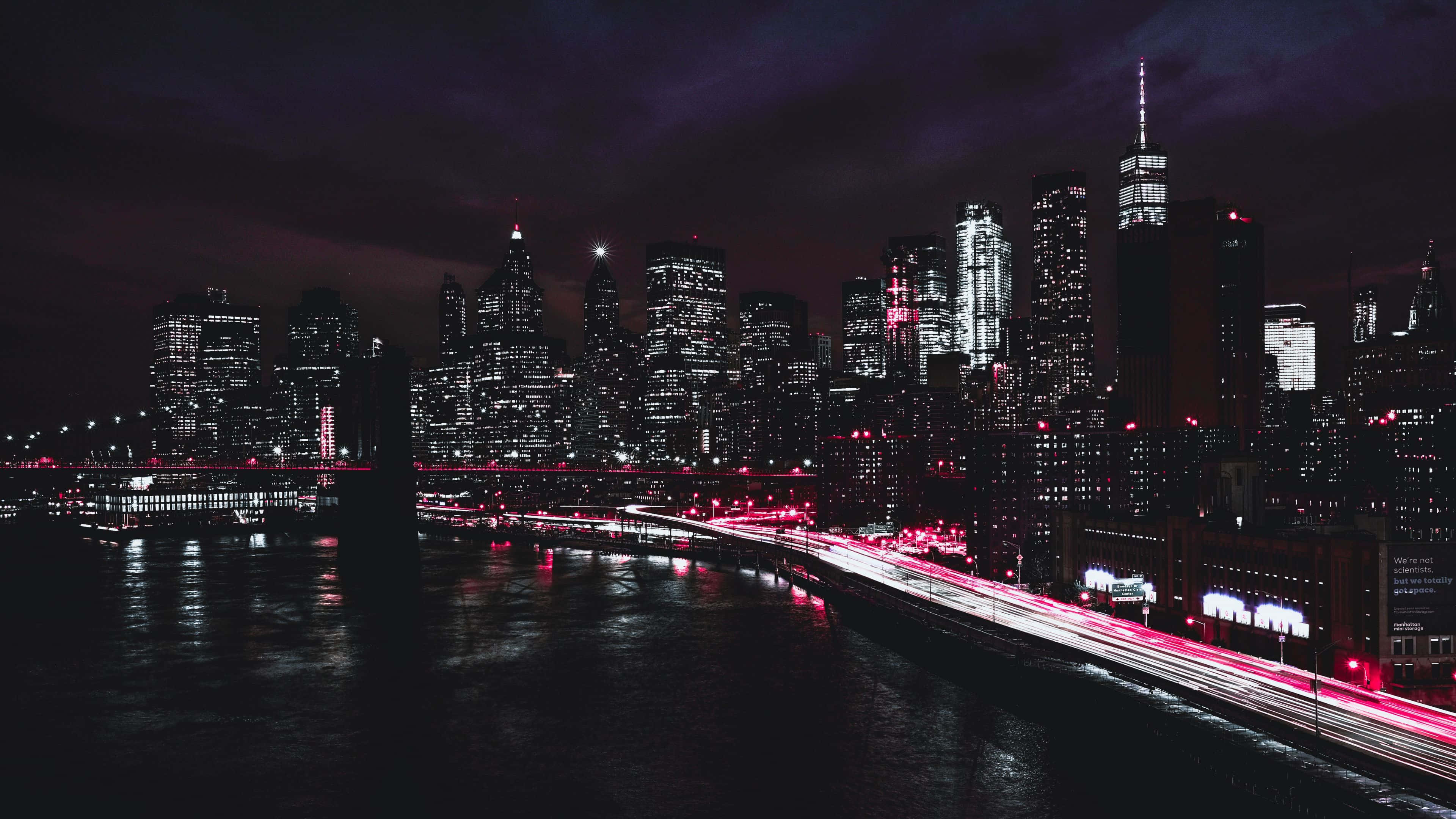 Skyscraper 桌布 壁紙 — 充滿活力的夜景，閃爍的摩天大樓和紅色車燈在黑暗的水面上形成條紋倒影。