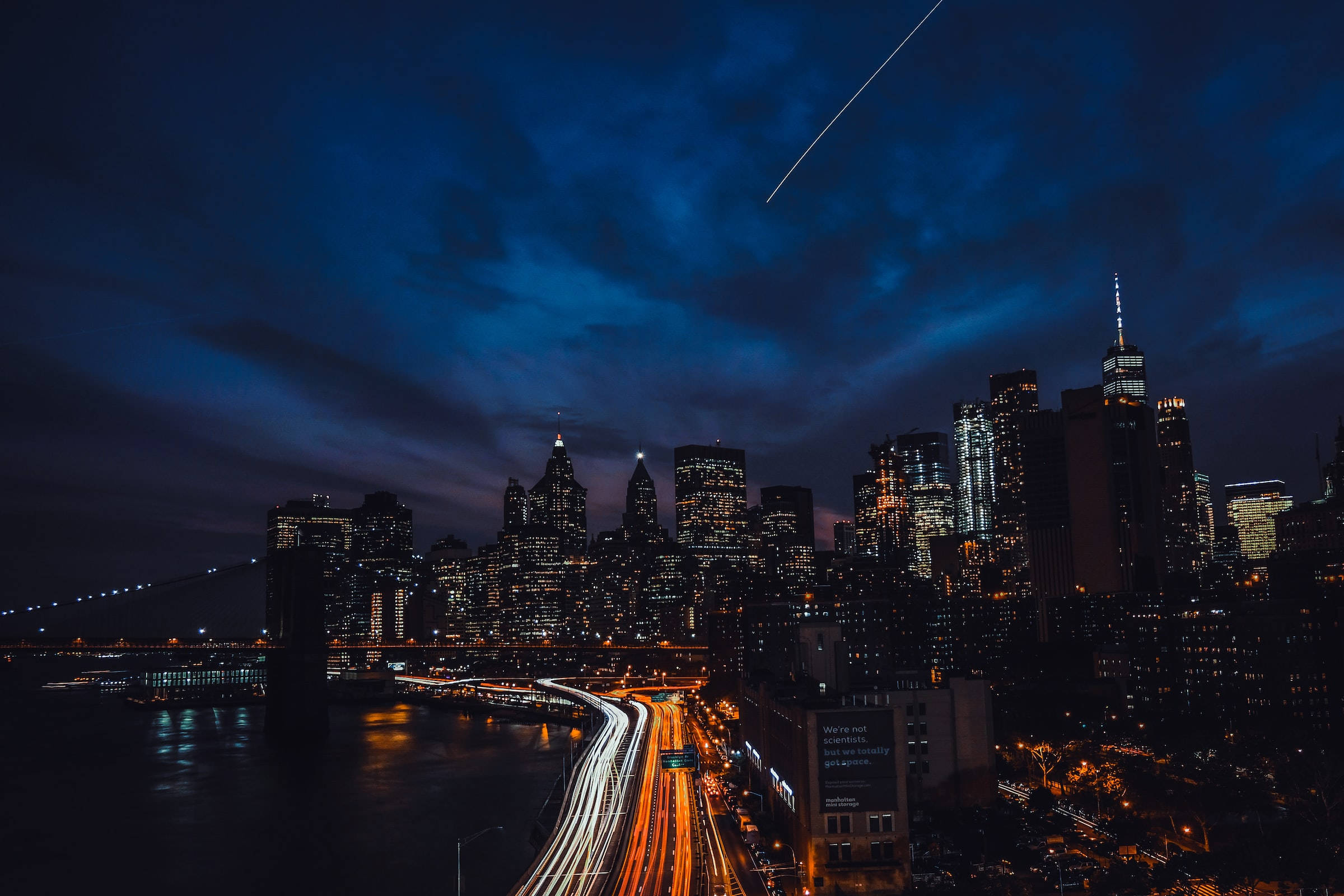 夜空 桌布 壁紙 — 充滿活力的夜景，閃爍的摩天大樓和流動的交通燈光，在深藍色的天空下有一條明亮的流星軌跡。