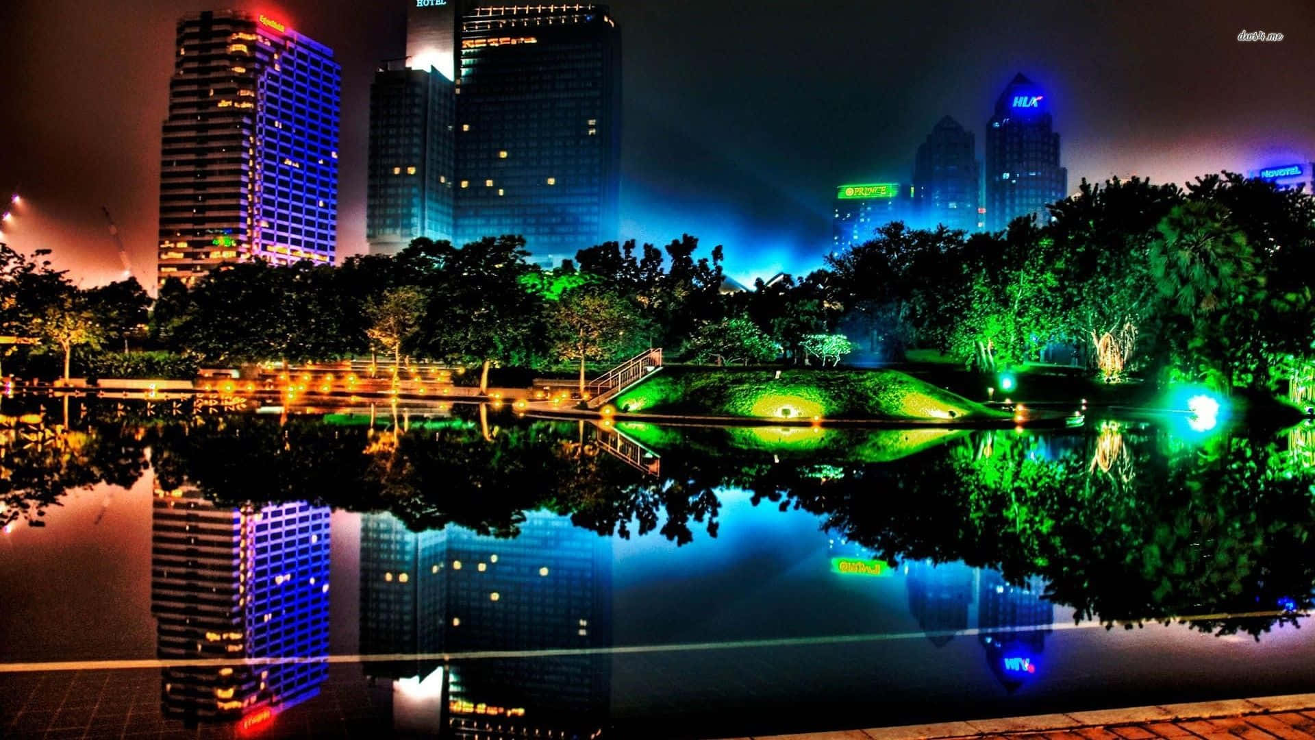 3d City 桌布 壁紙 — 充滿活力的夜景，霓虹燈閃爍的摩天大樓倒映在平靜的池塘中，周圍環繞著發光的綠色樹木。