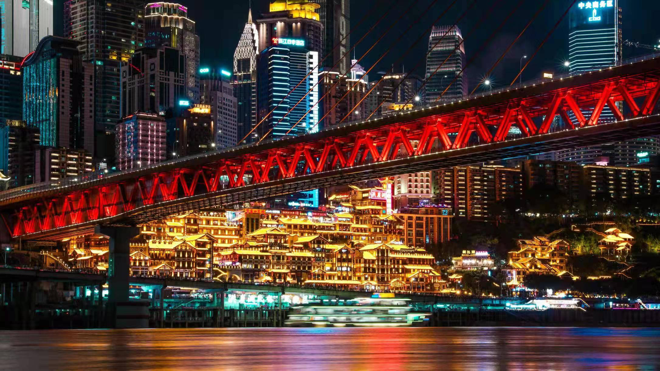 Chongqing 桌布 壁紙 — 充滿活力的夜景城市景觀，一座發光的紅色橋樑橫跨河流，下方是燈火通明的摩天大樓和傳統建築。