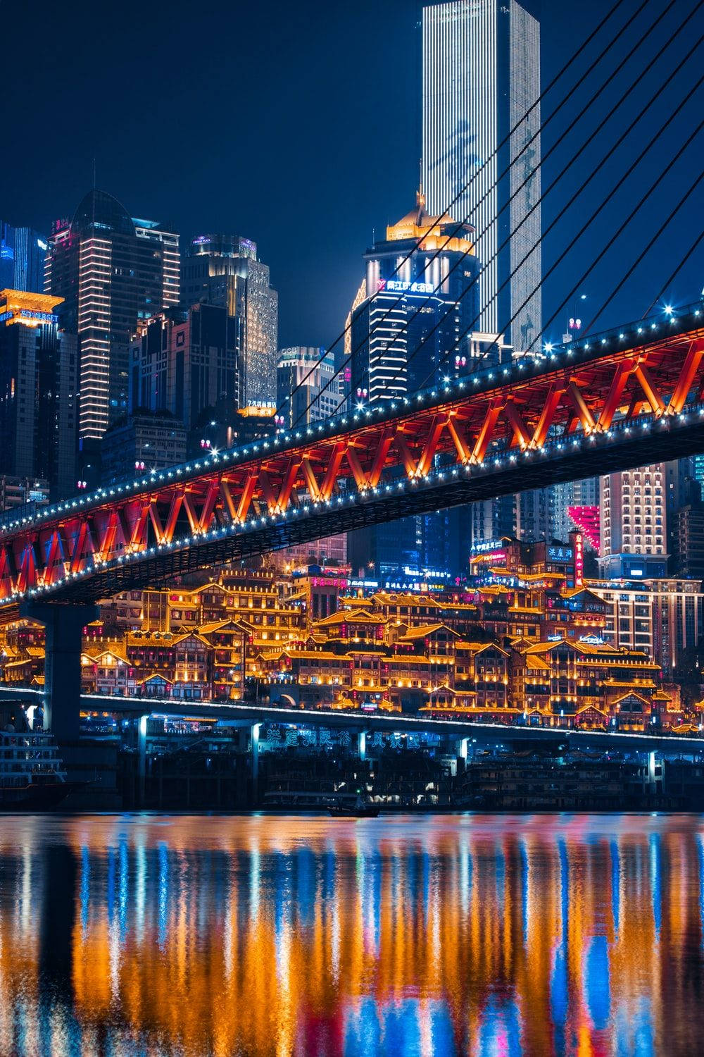 Chongqing 桌布 壁紙 — 充滿活力的夜景城市景觀，一座發光的紅色橋樑橫跨河流，倒映著現代摩天大樓和傳統建築的霓虹燈光。