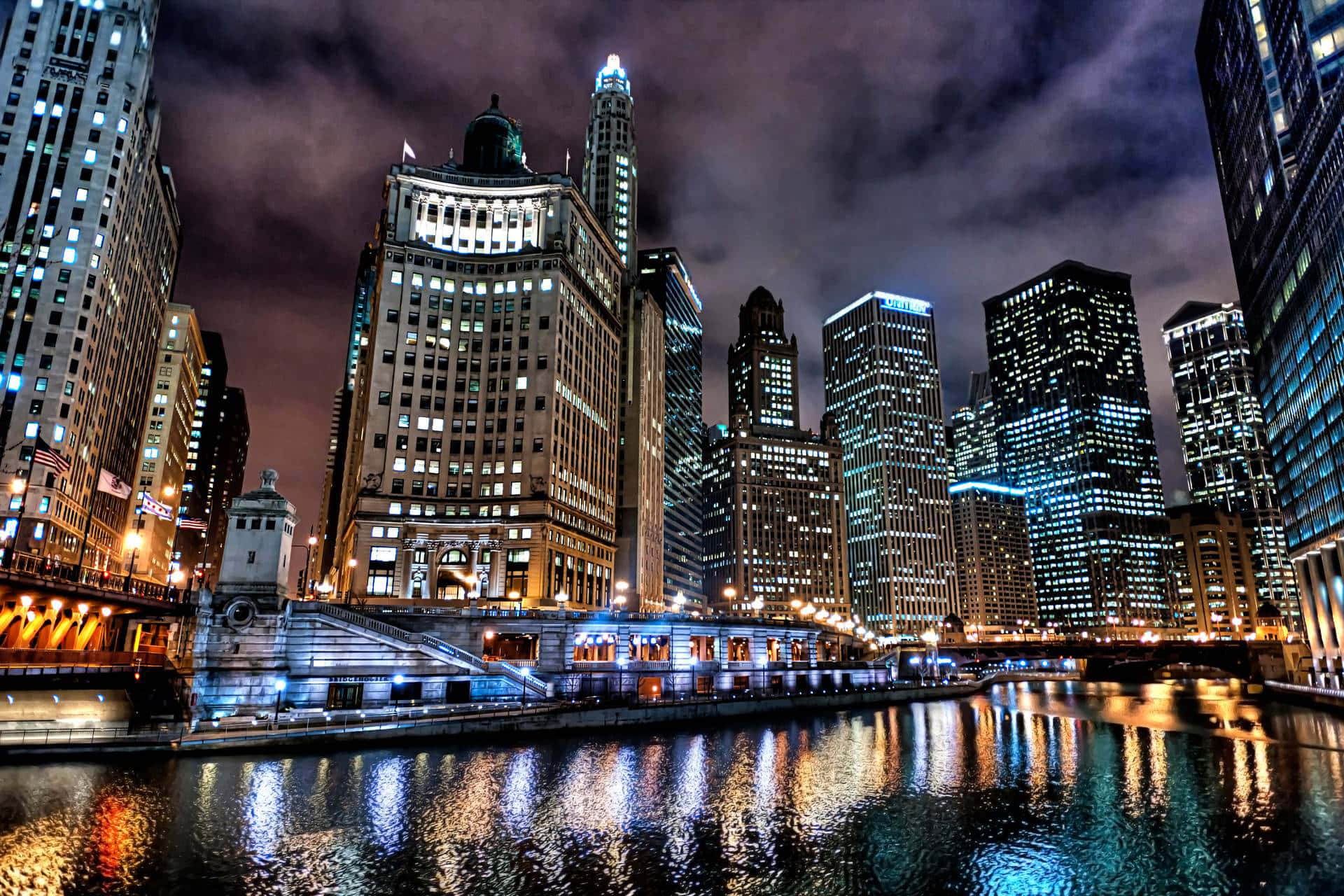 City Desktop 桌布 壁紙 — 充滿活力的夜景城市景觀，在陰天之下，明亮的摩天大樓倒映在黑暗的河流中。