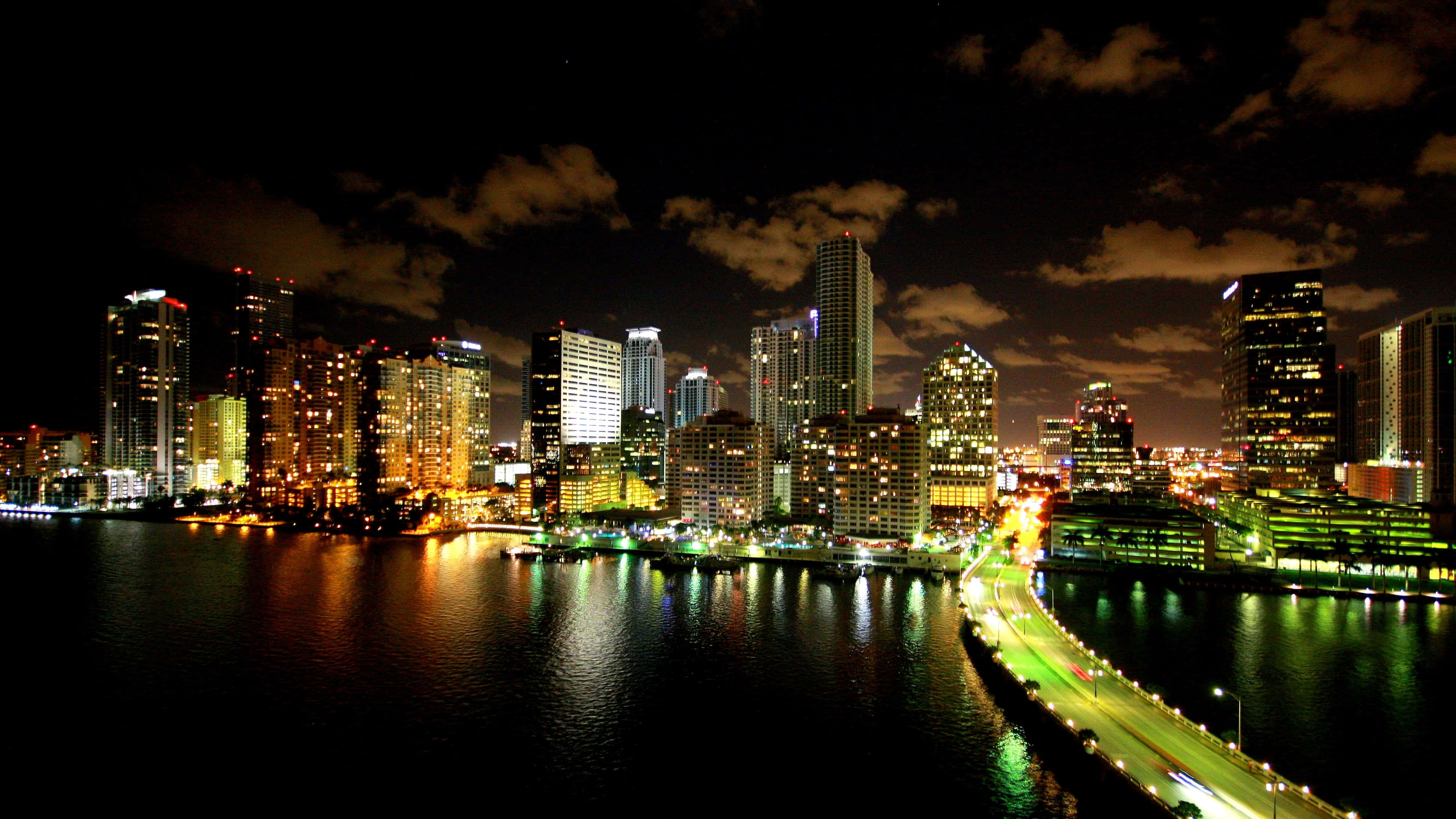 Miami 桌布 壁紙 — 充滿活力的夜景城市景觀，摩天大樓在陰天下的黑暗水面上閃爍倒影。