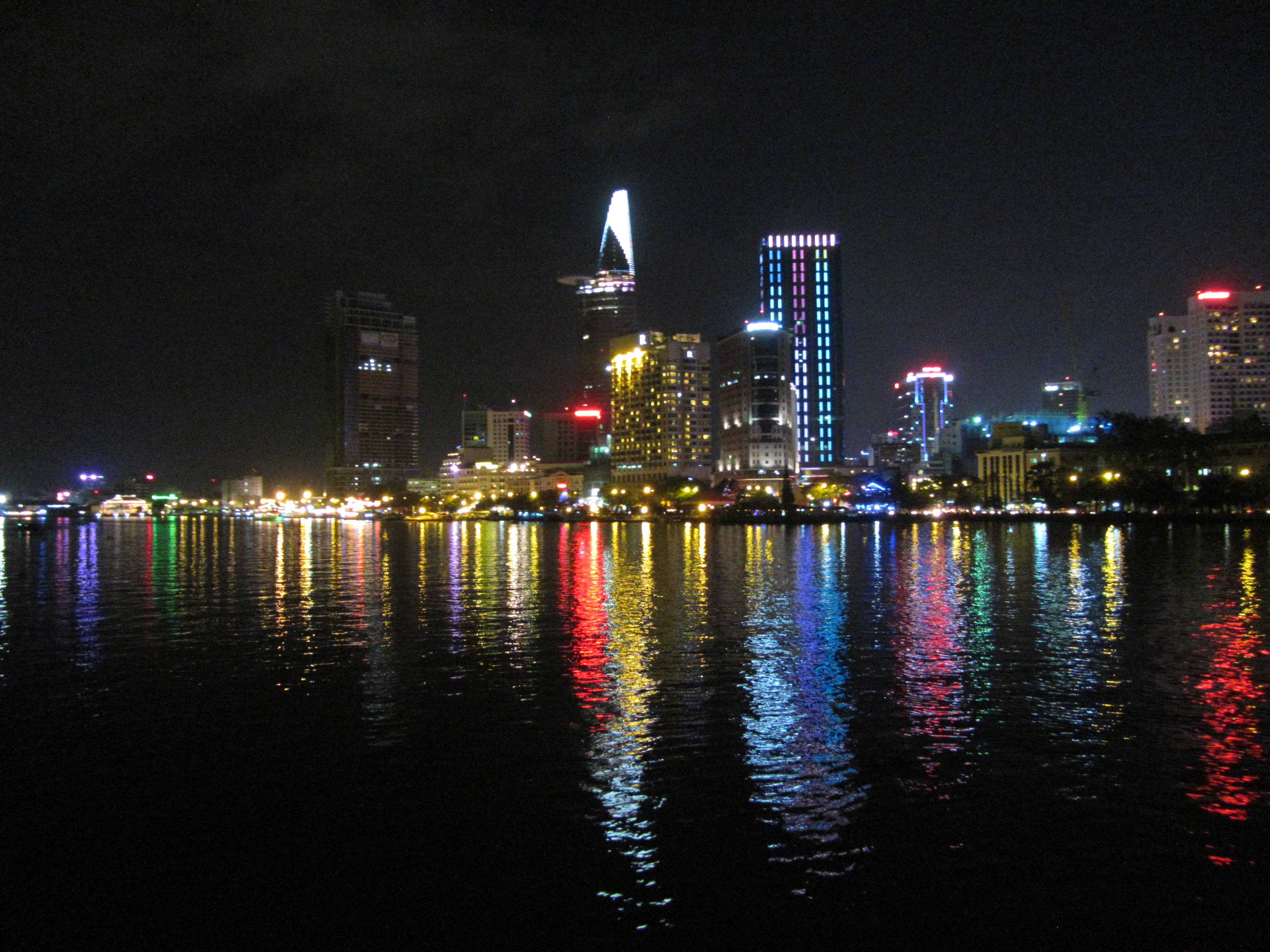 Vietnam 桌布 壁紙 — 充滿活力的夜景城市景觀，摩天大樓在無星的天空下映照在黑暗的水面上。