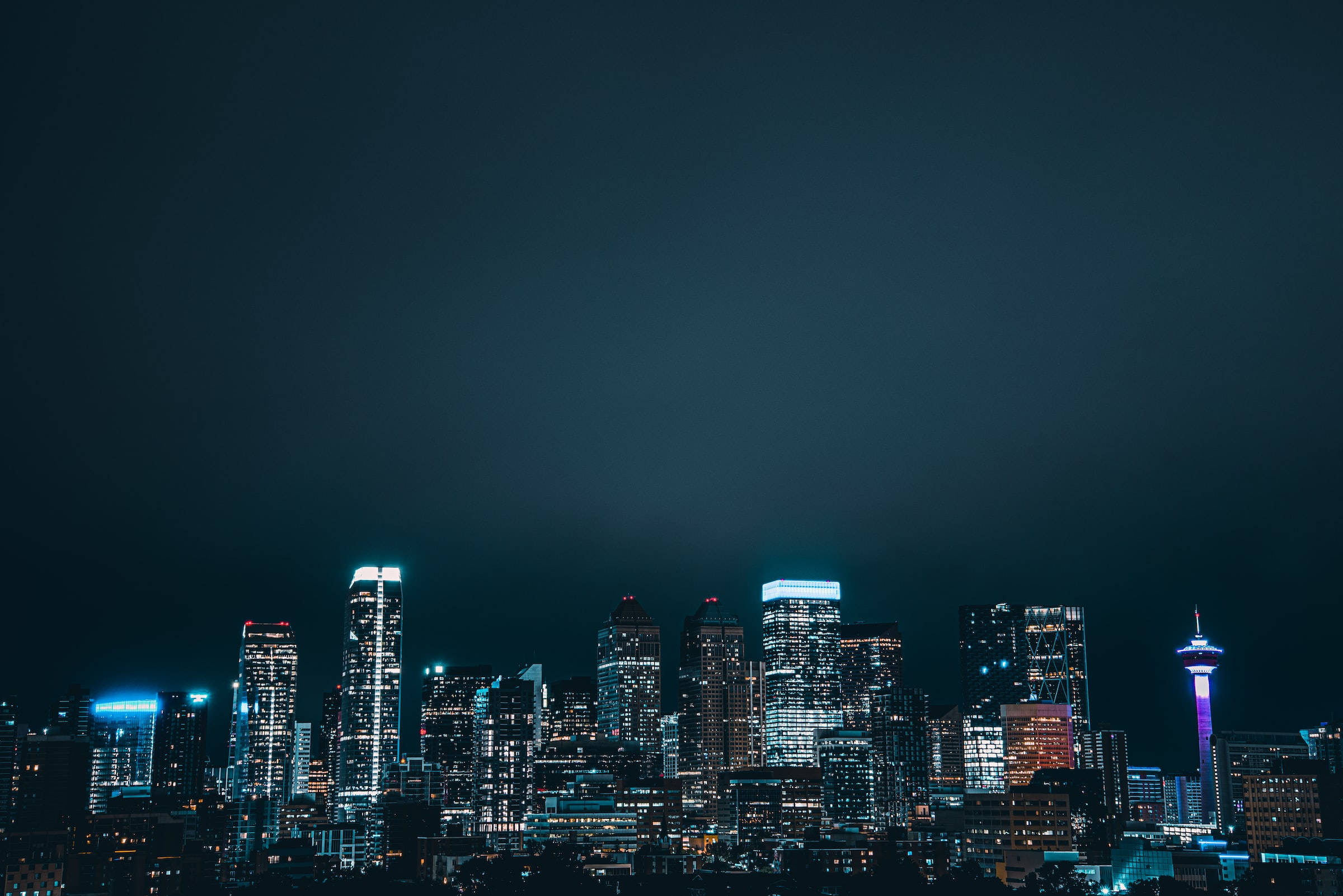 Night Aesthetic 桌布 壁紙 — 充滿活力的夜景城市景觀，摩天大樓燈火通明，高塔在深藍色天空下閃耀。