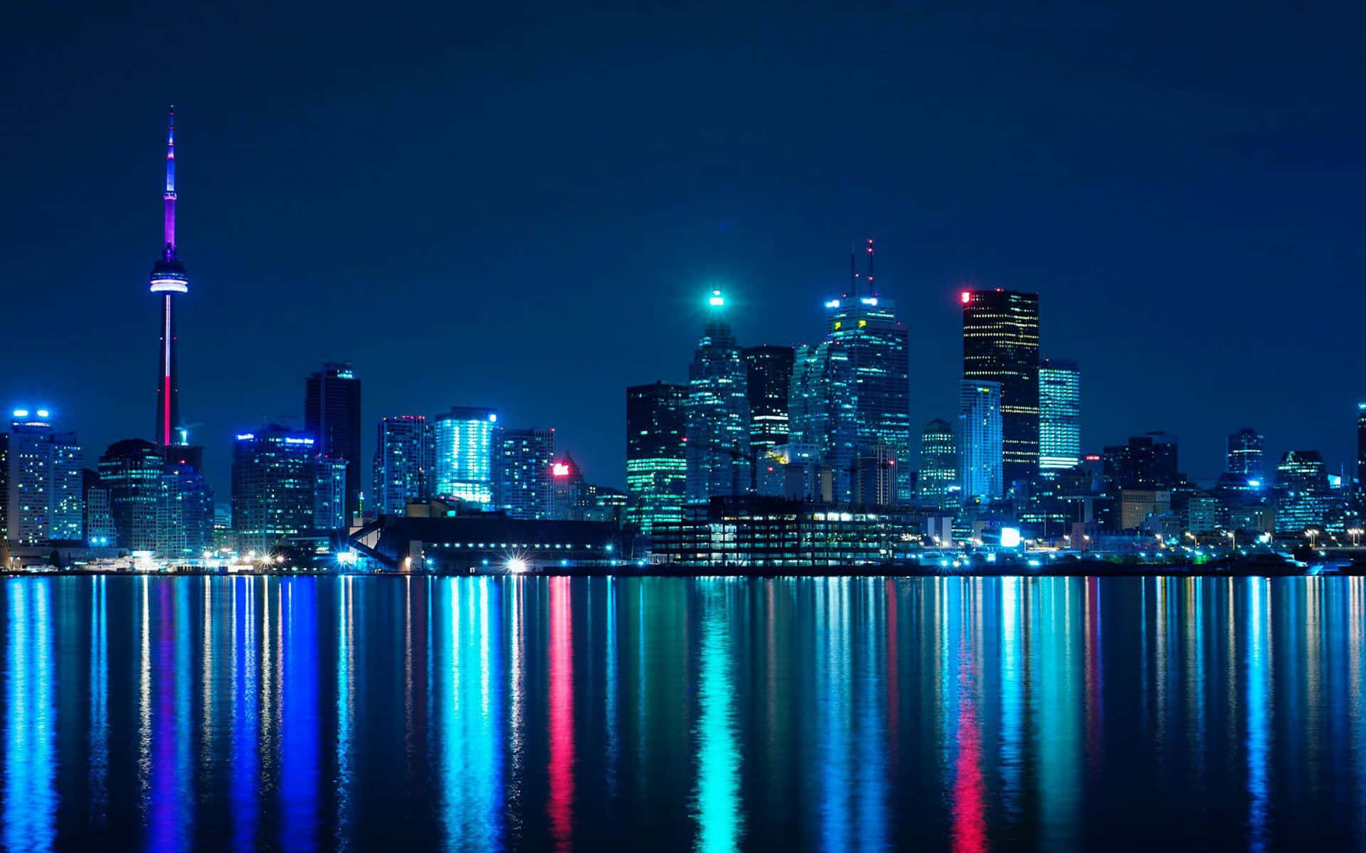 Toronto Skyline 桌布 壁紙 — 充滿活力的夜景城市景觀，有燈火通明的摩天大樓和發光的CN塔倒映在平靜的水面上。