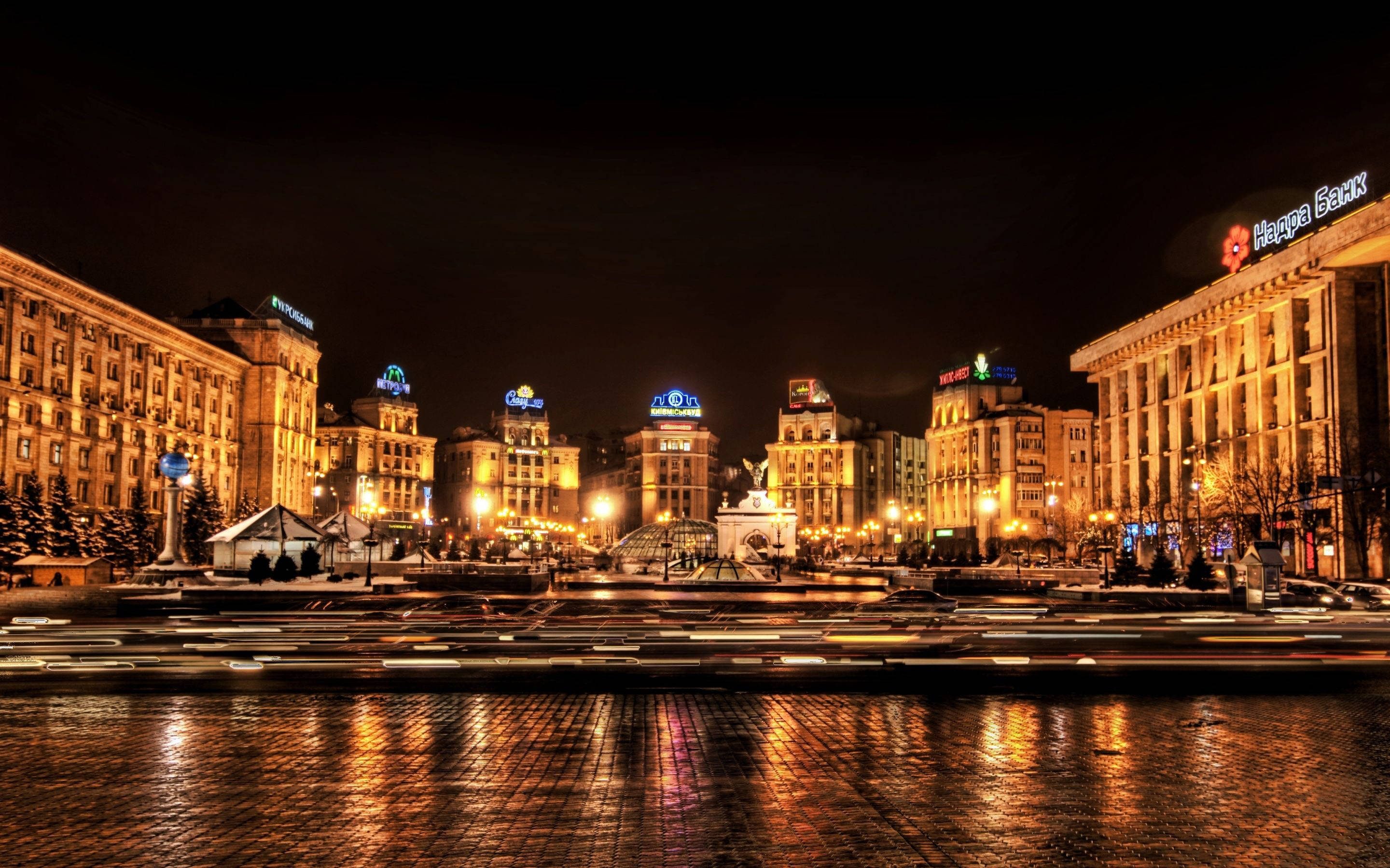 Ukraine 桌布 壁紙 — 充滿活力的夜景城市景觀，有燈火通明的建築物和車燈在濕漉漉的路面上反射出的條紋。