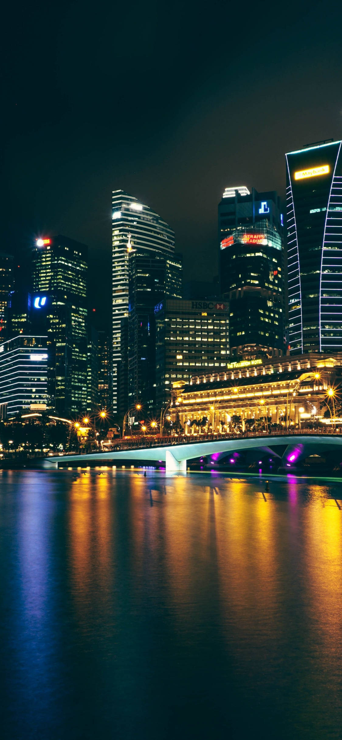 Singapore 桌布 壁紙 — 充滿活力的夜景城市景觀，有燈火通明的摩天大樓和一座在平靜水面上倒映的發光橋樑。