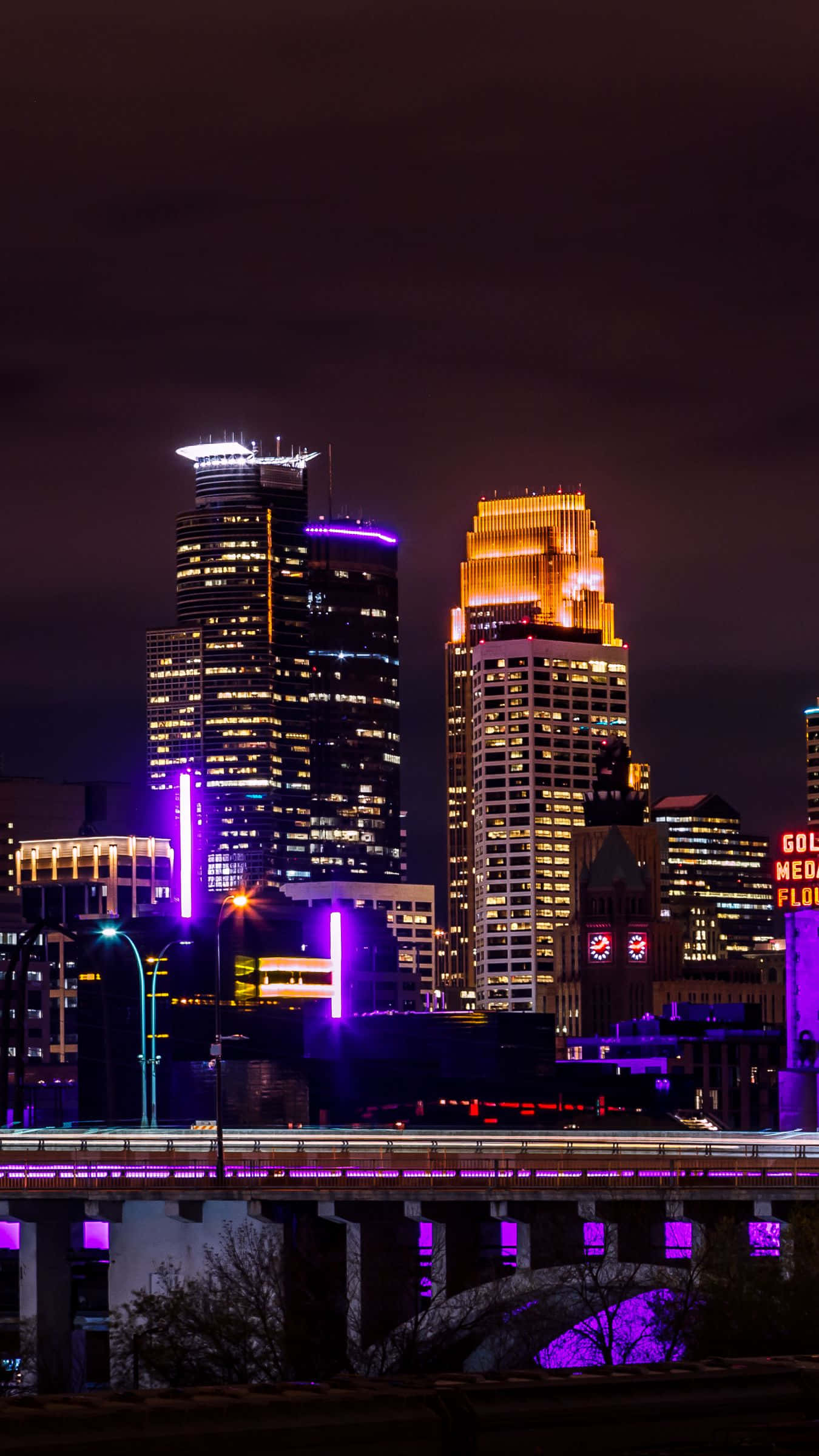 Panorama 桌布 壁紙 — 充滿活力的夜景城市景觀，有發光的摩天大樓和一座在黑暗天空下河流上閃爍的橋樑。