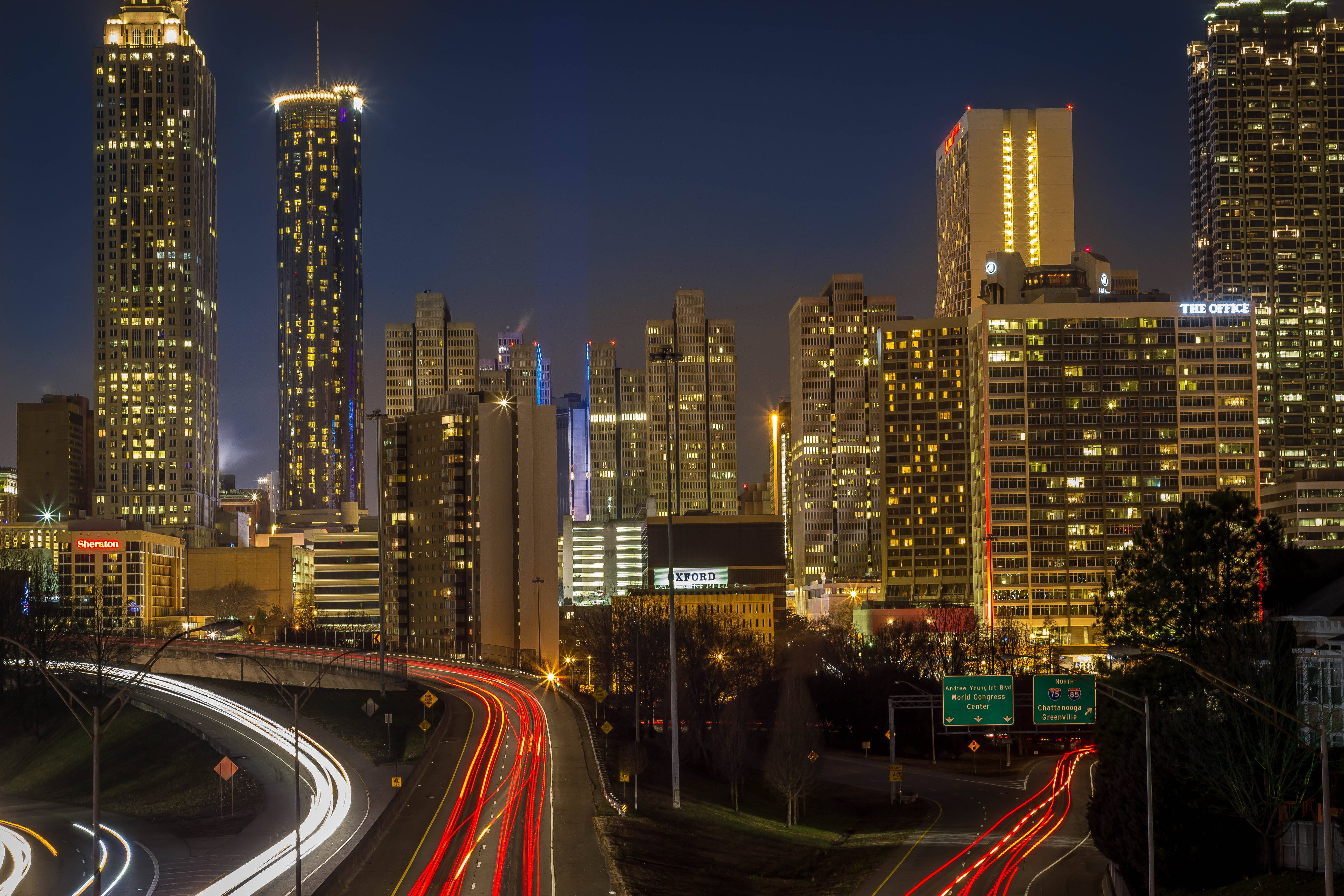 Skyscraper 桌布 壁紙 — 充滿活力的夜景城市景觀，有發光的摩天大樓和彎曲高速公路上車流留下的光跡。