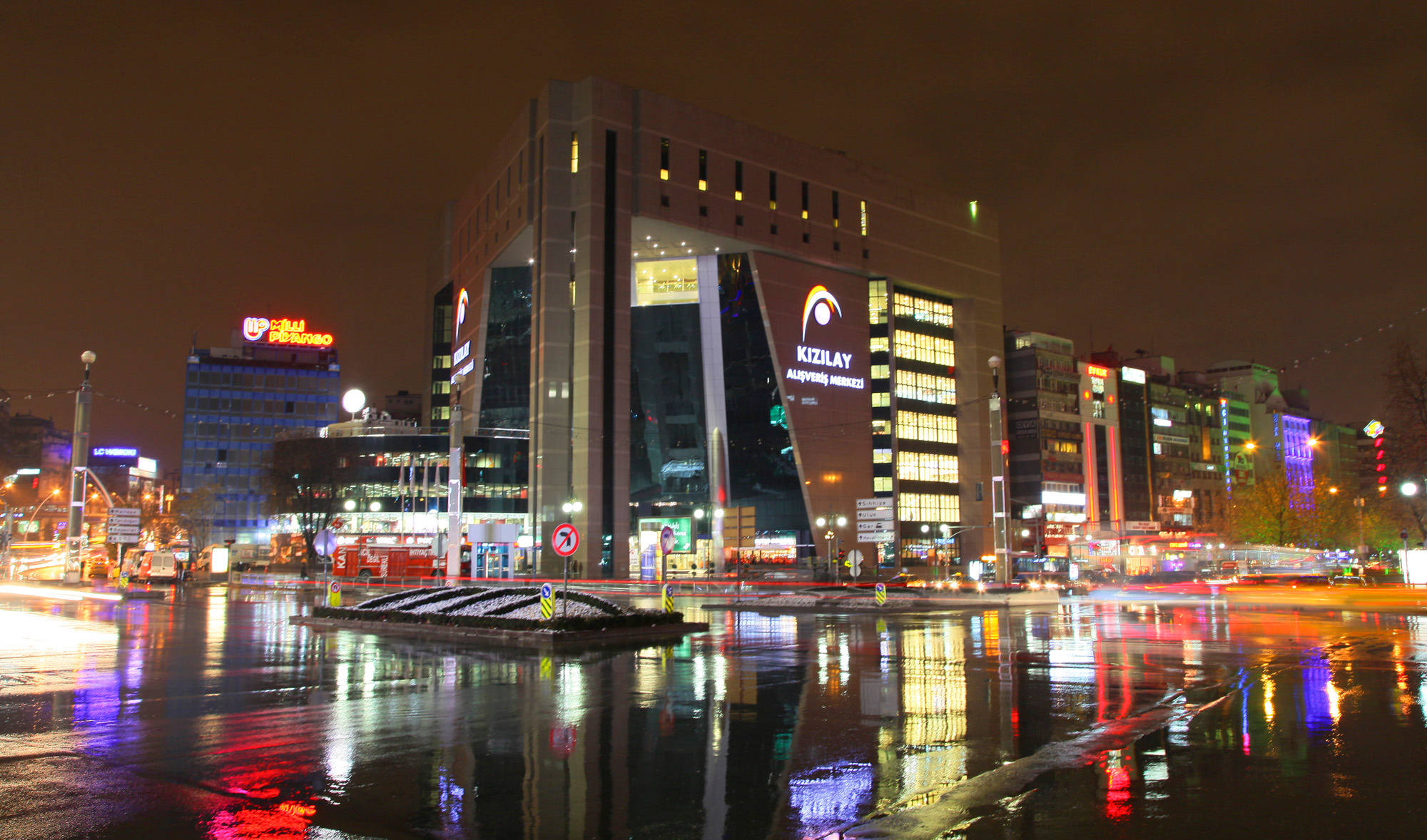Ankara 桌布 壁紙 — 充滿活力的夜景城市景觀，濕漉漉的街道反射著高聳建築物和發光招牌的霓虹燈光。