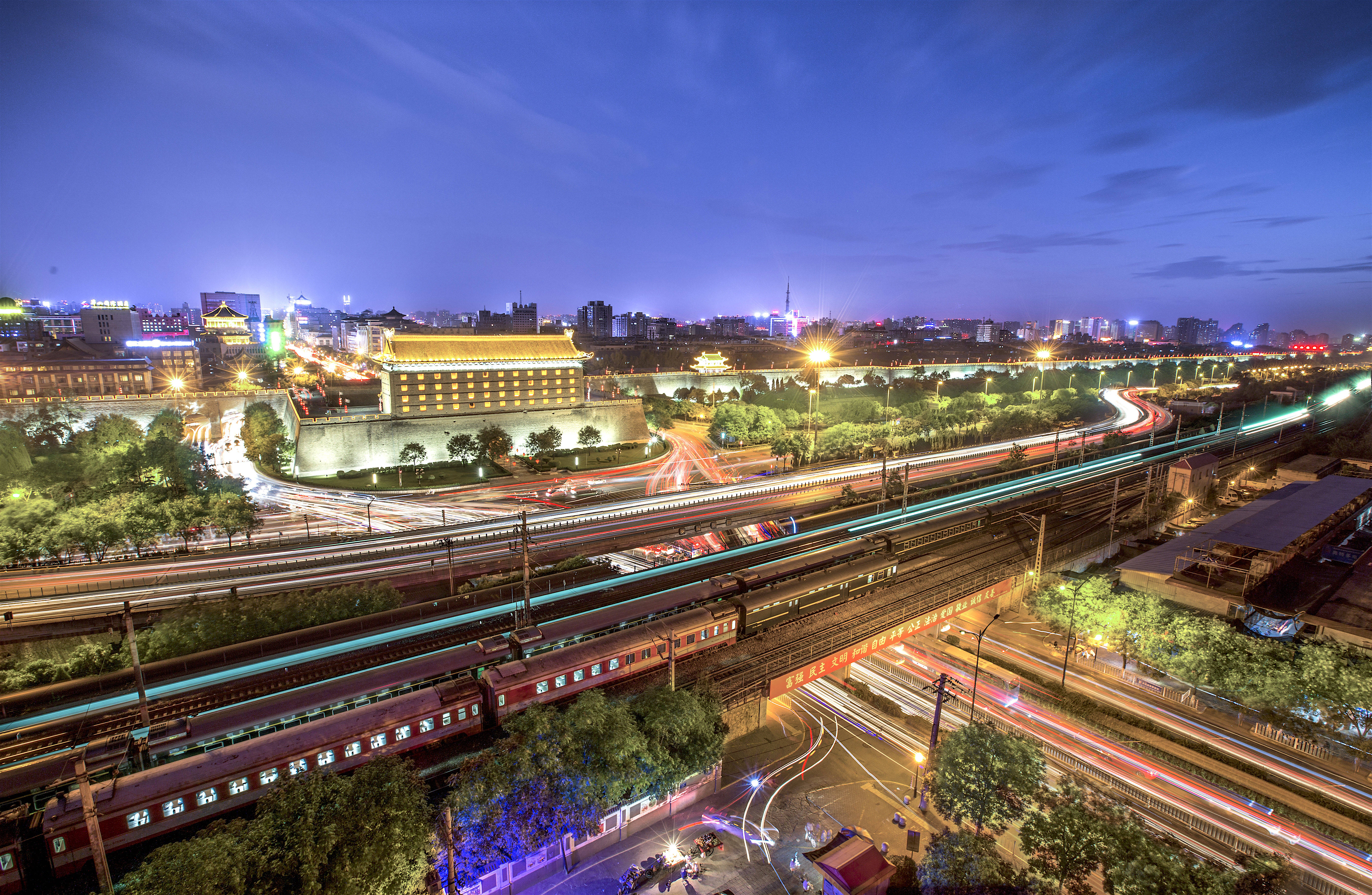 Xian 桌布 壁紙 — 充滿活力的夜景城市景觀，燈光在高速公路上閃爍，歷史城牆在深藍色天空下被照亮。