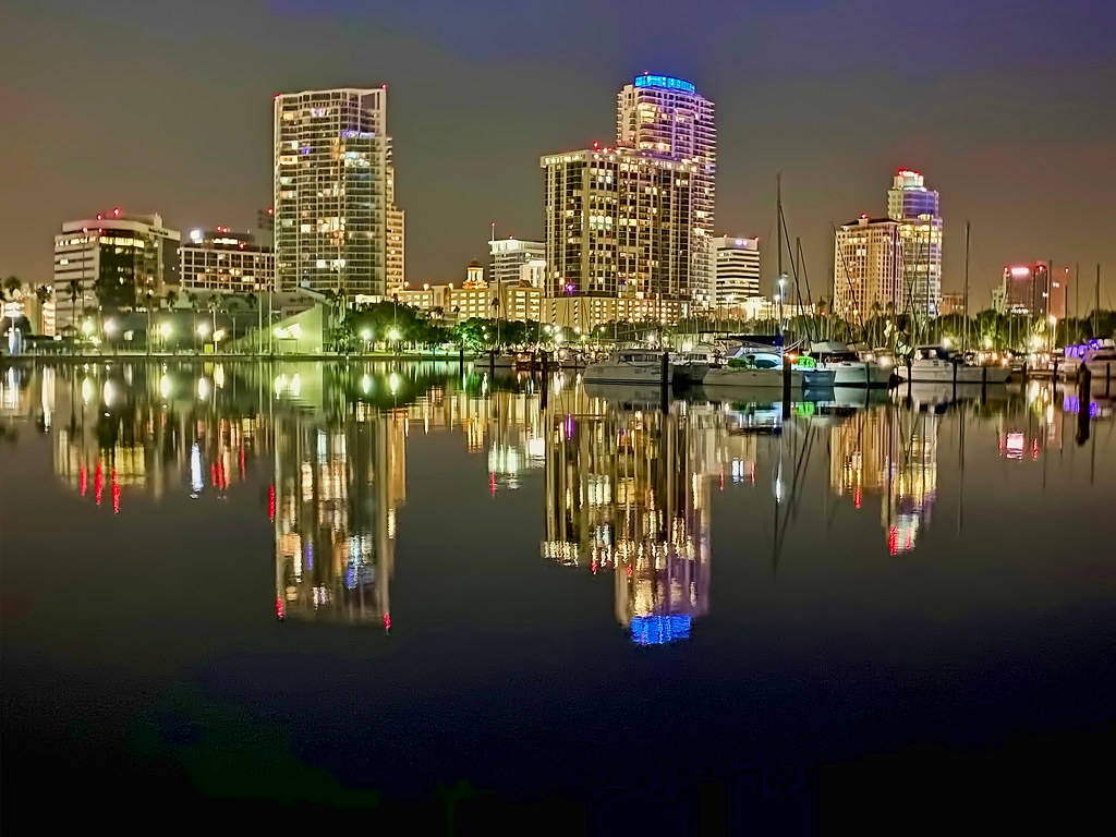 Evening 桌布 壁紙 — 充滿活力的夜景城市景觀，燈火通明的摩天大樓和船隻倒映在平靜的水面上。