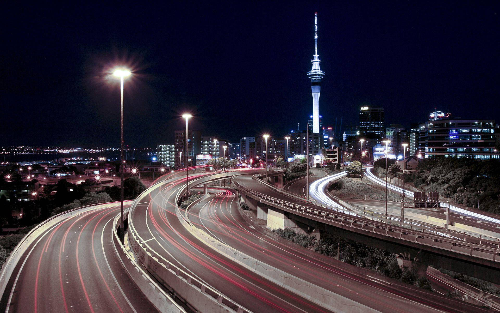 New 桌布 壁紙 — 充滿活力的夜景城市景觀，特色是發光的高速公路、流動的車燈，以及一座高聳的照明摩天大樓，映襯著黑暗的天空。