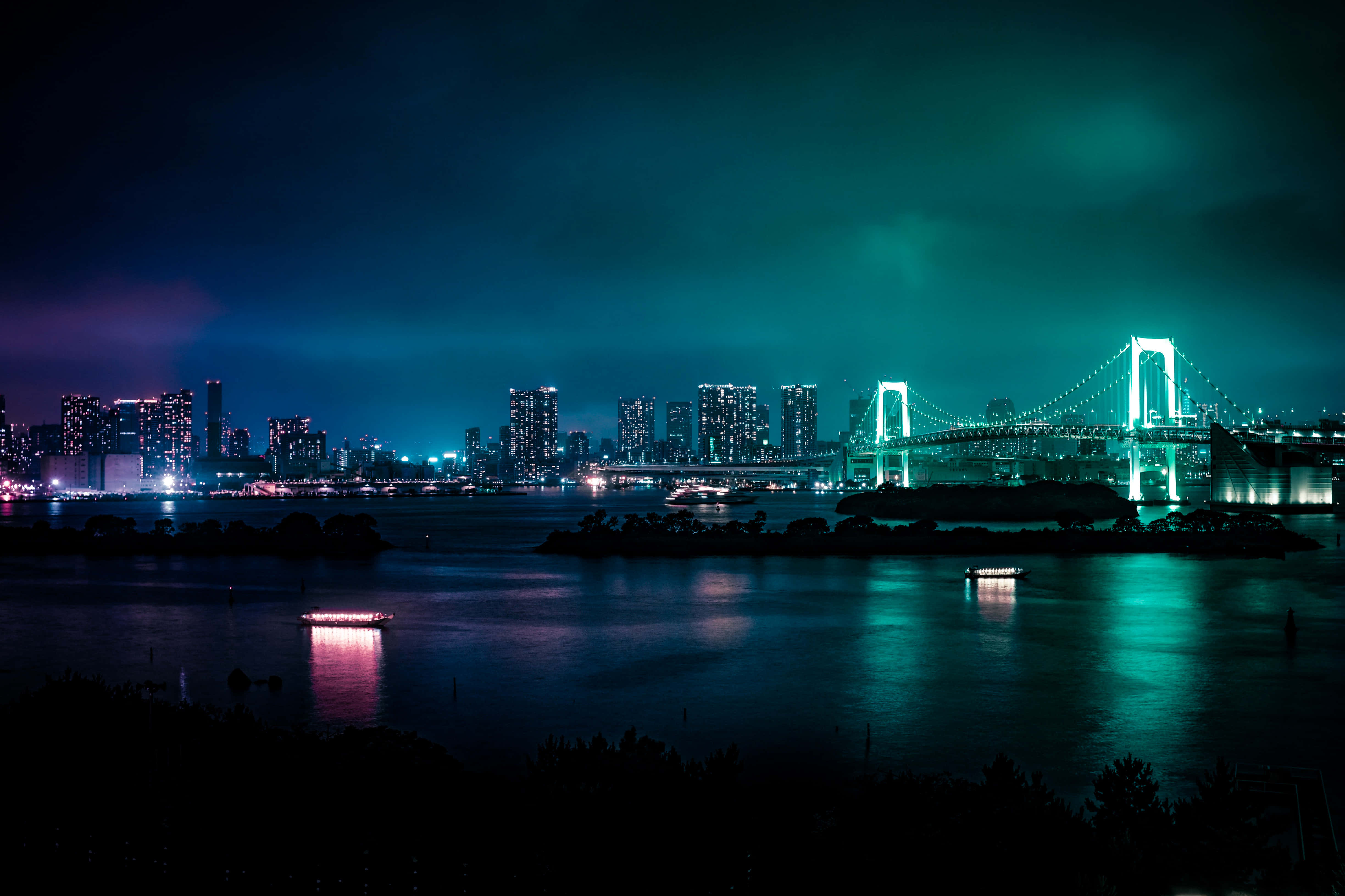 城市風景 桌布 壁紙 — 充滿活力的夜景城市景觀，特色是發光的彩虹橋橫跨水面，有船隻和摩天大樓，在青綠色的天空下。
