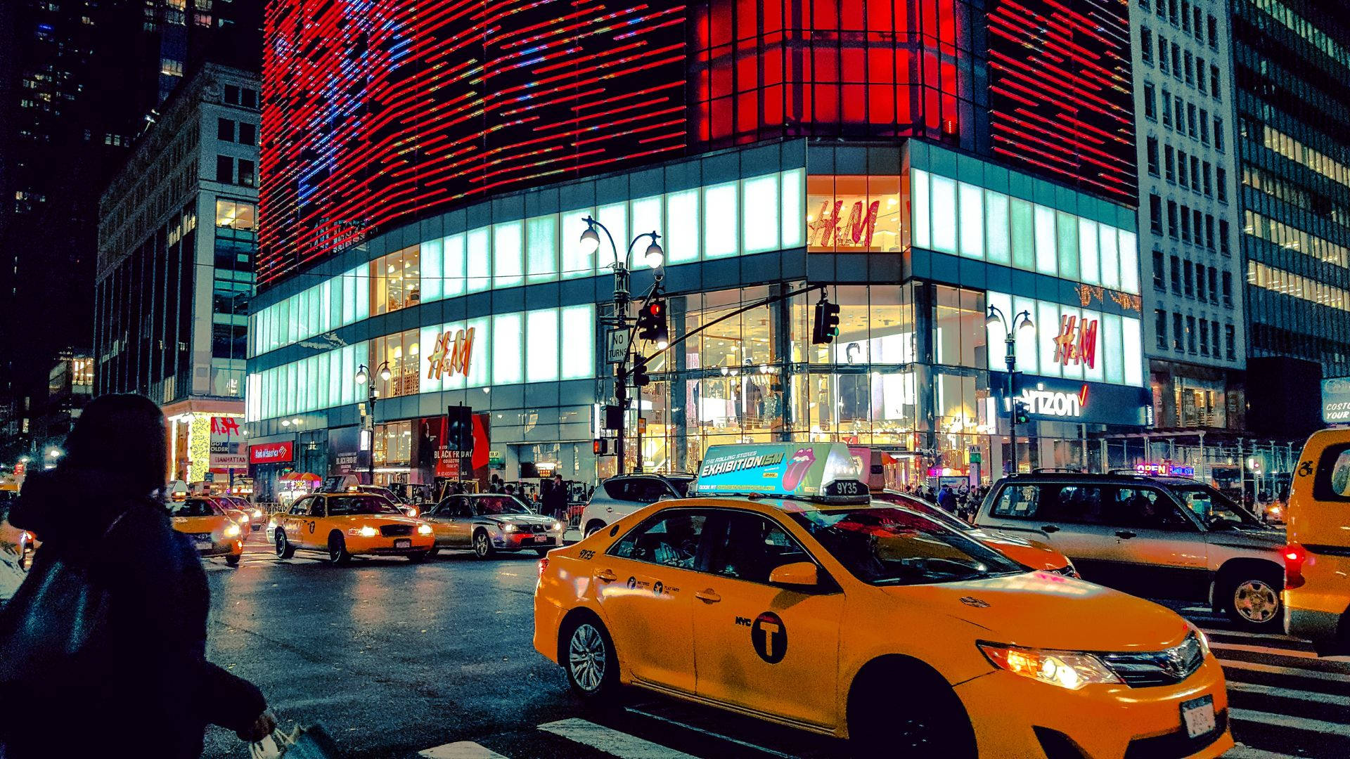 taxi 桌布 壁紙 — 充滿活力的夜景城市景觀，特色是黃色的士和帶有H&M標誌的紅色發光建築。