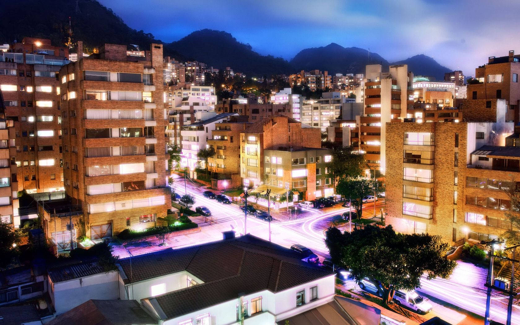 Bogota 桌布 壁紙 — 充滿活力的夜景城市景觀，發光的建築物和流動的車燈，以黑暗的山脈為背景。