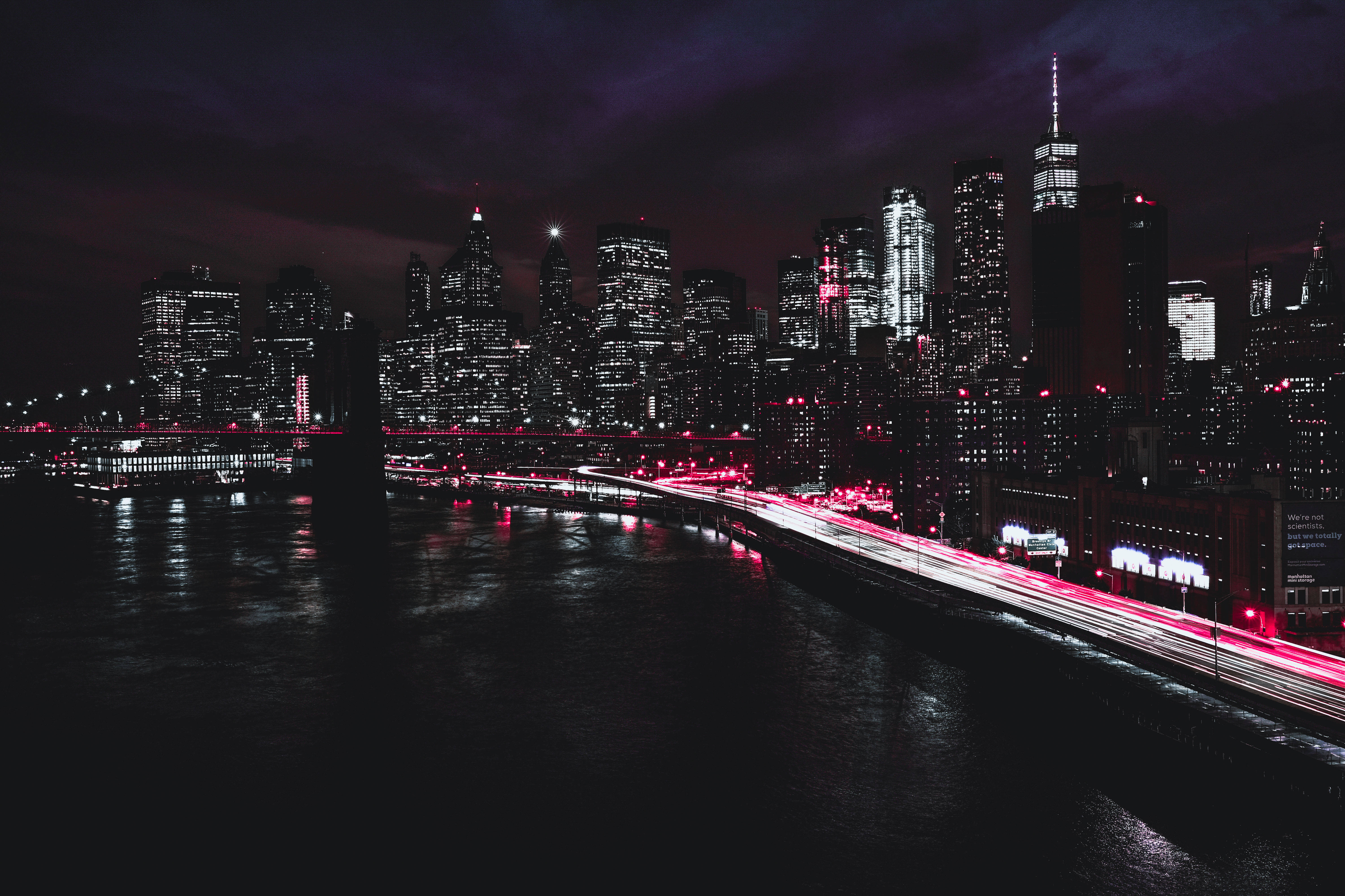 City Night 桌布 壁紙 — 充滿活力的夜景城市景觀，發光的摩天大樓和紅色車燈在黑暗的水面上反射。