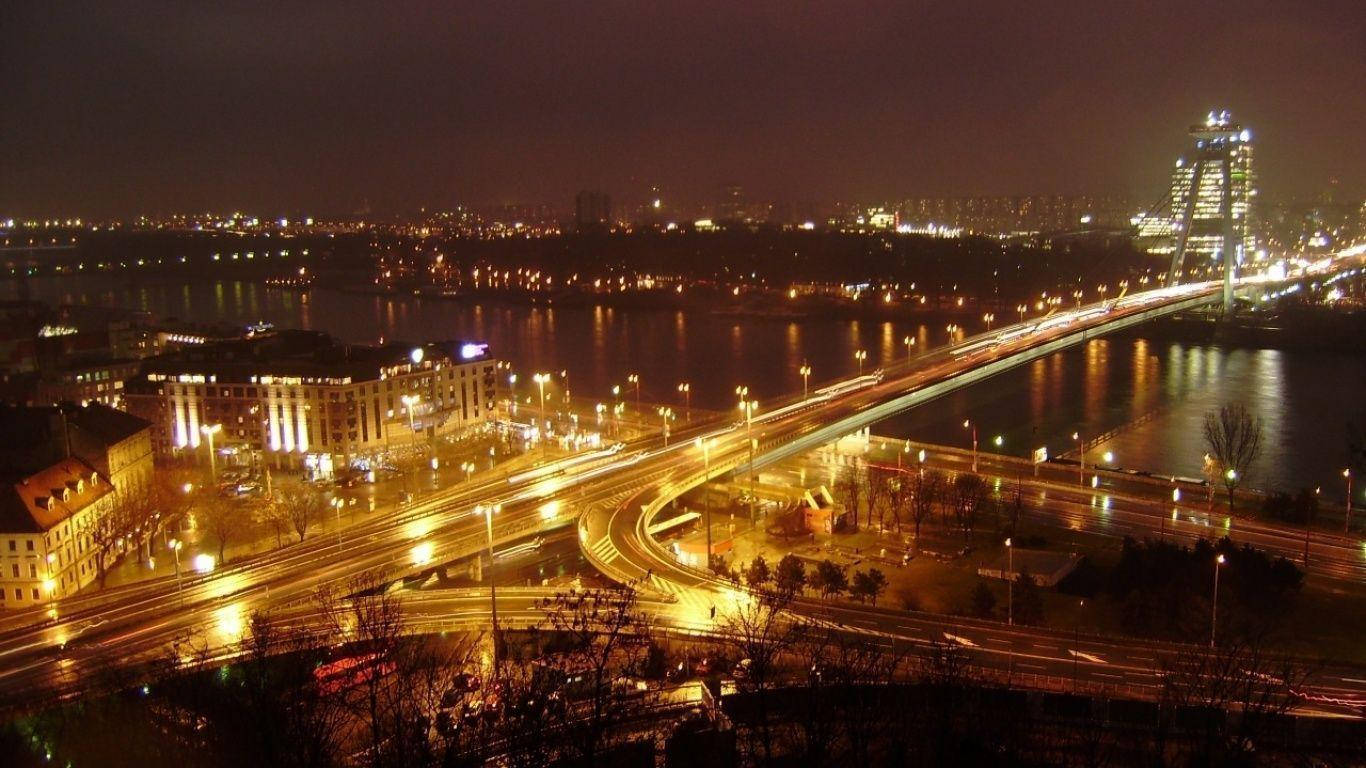 Slovakia 桌布 壁紙 — 充滿活力的夜景城市景觀，發光的燈光倒映在河上，車流的光跡流過橋樑。