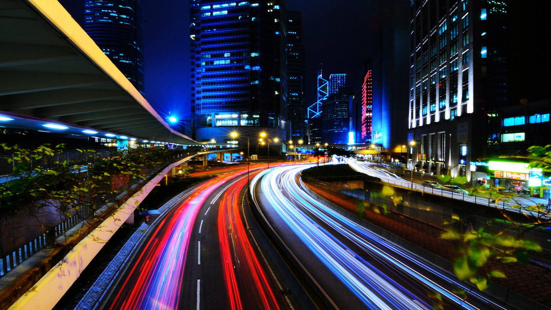 X 桌布 壁紙 — 充滿活力的夜景城市景觀，車流在聳立的照明摩天大樓下流動，留下紅色和藍色的光跡。