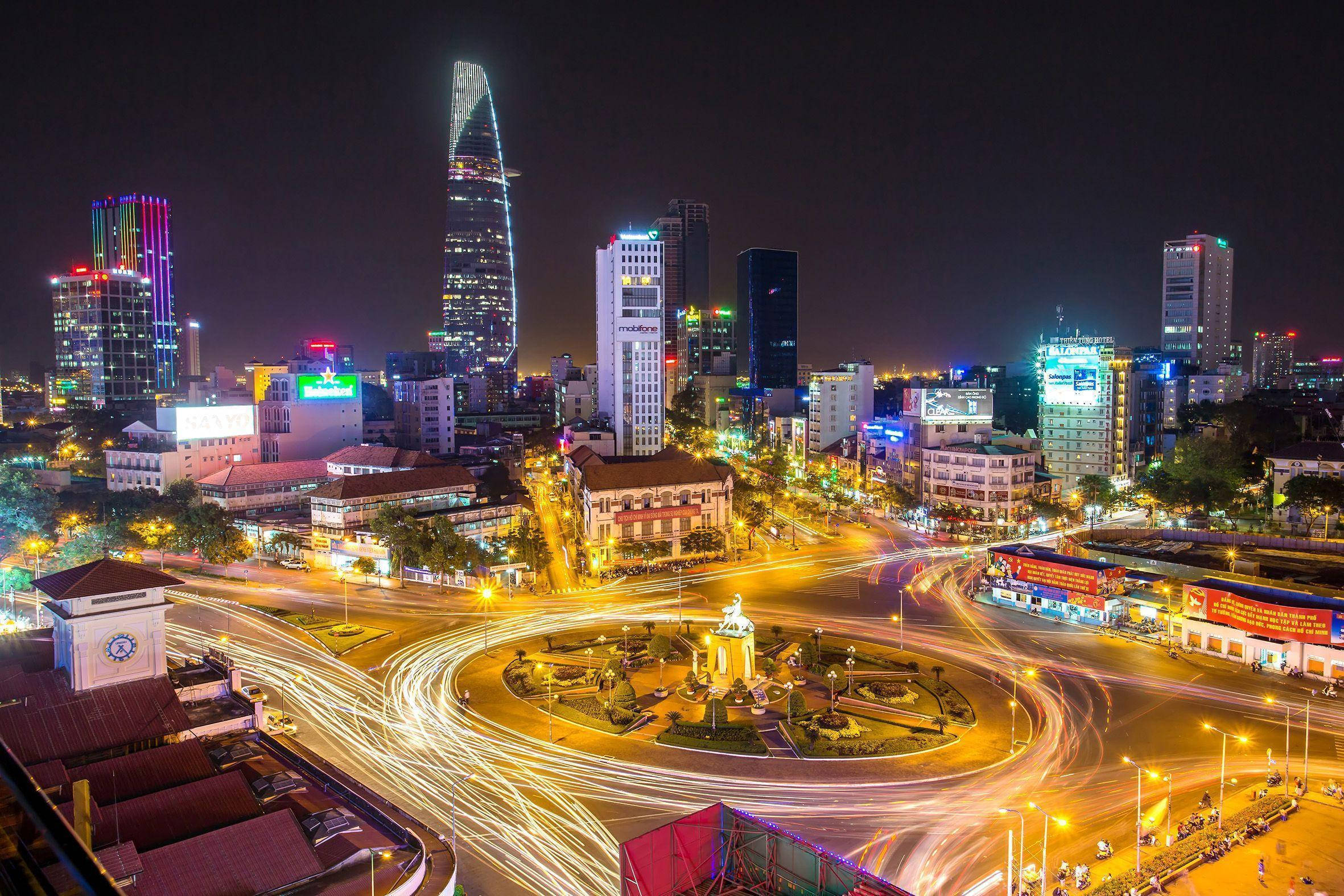 城市 桌布 壁紙 — 充滿活力的夜景城市景觀，閃爍的摩天大樓和圍繞中央紀念碑旋轉的車流光跡。