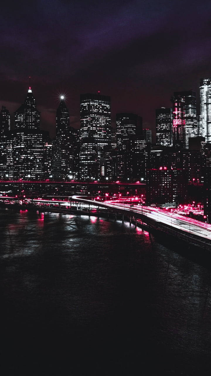New 桌布 壁紙 — 充滿活力的夜景城市景觀，閃爍的摩天大樓和粉紅色燈光的橋樑倒映在黑暗的水面上。