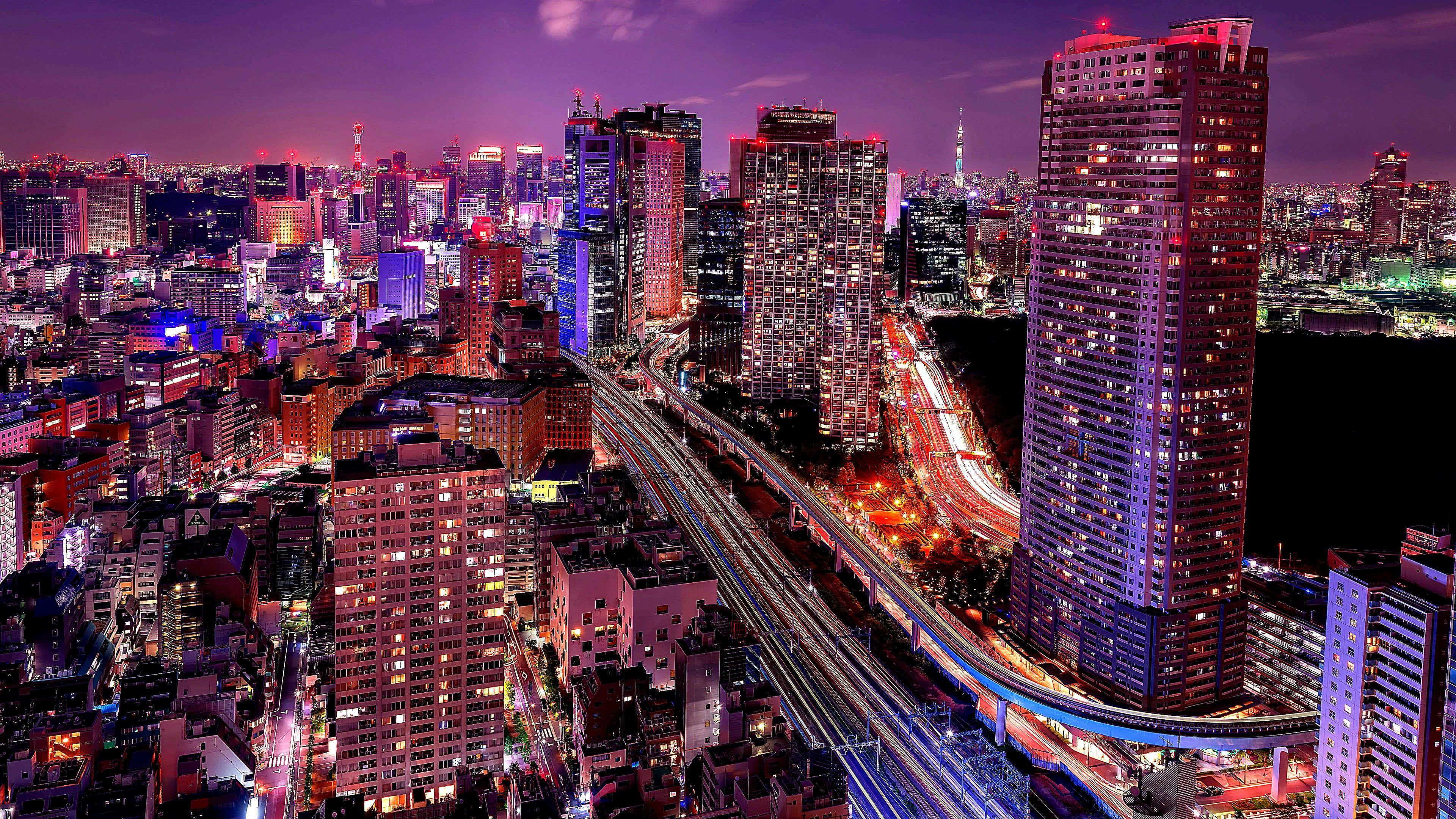 東京 桌布 壁紙 — 充滿活力的夜景城市景觀，閃爍的摩天大樓和高架高速公路上的車流光跡。