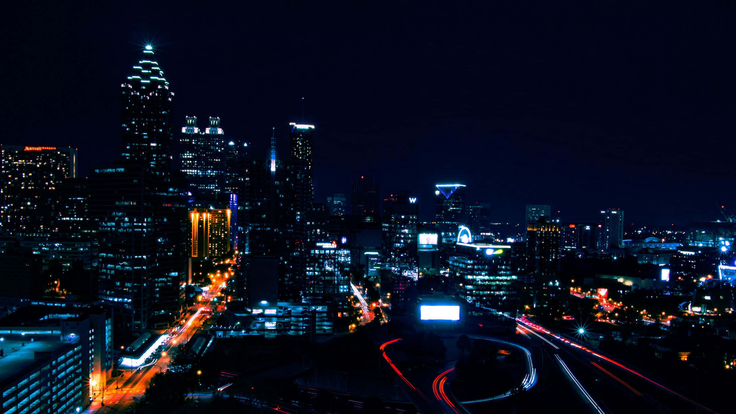 City Lights 桌布 壁紙 — 充滿活力的夜景城市景觀，閃爍的摩天大樓和下方交通的光跡。