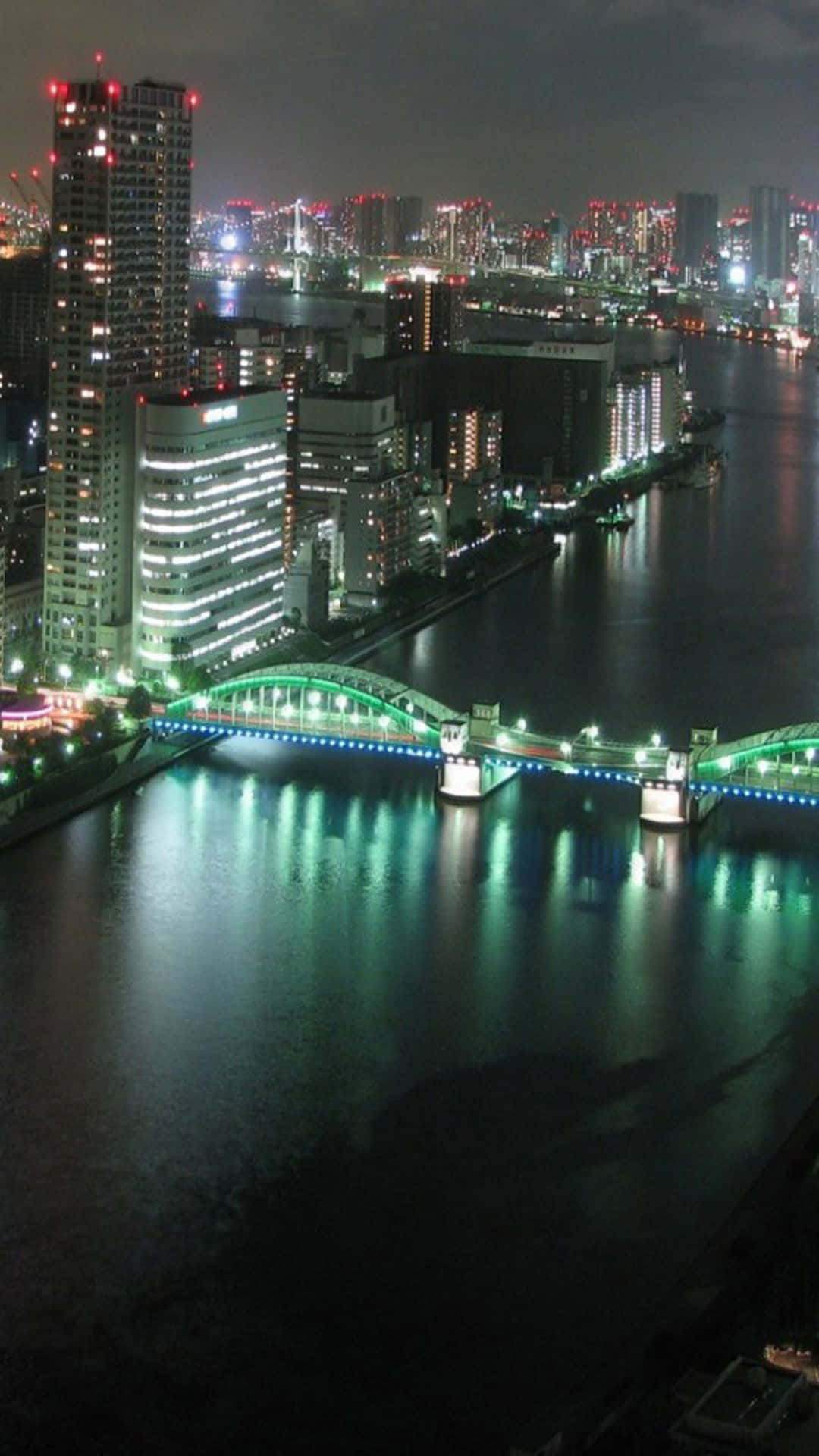 Lit iPhone 桌布 壁紙 — 充滿活力的夜景城市景觀，閃爍的摩天大樓和霓虹燈橋樑倒映在平靜的水面上。