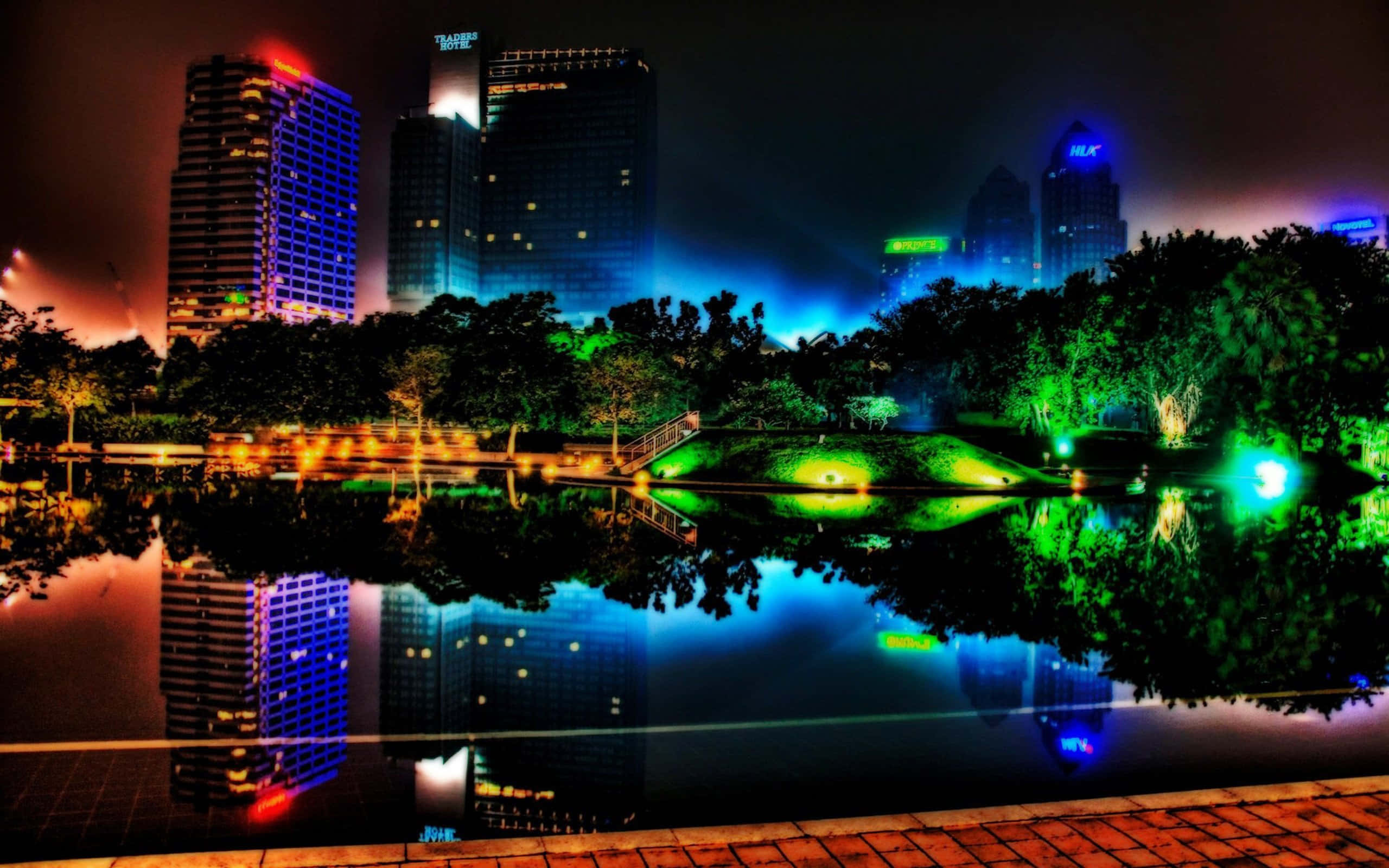 Chilly Night 桌布 壁紙 — 充滿活力的夜景城市景觀，霓虹燈閃爍的摩天大樓倒映在平靜的池塘中，周圍環繞著發光的綠色樹木。