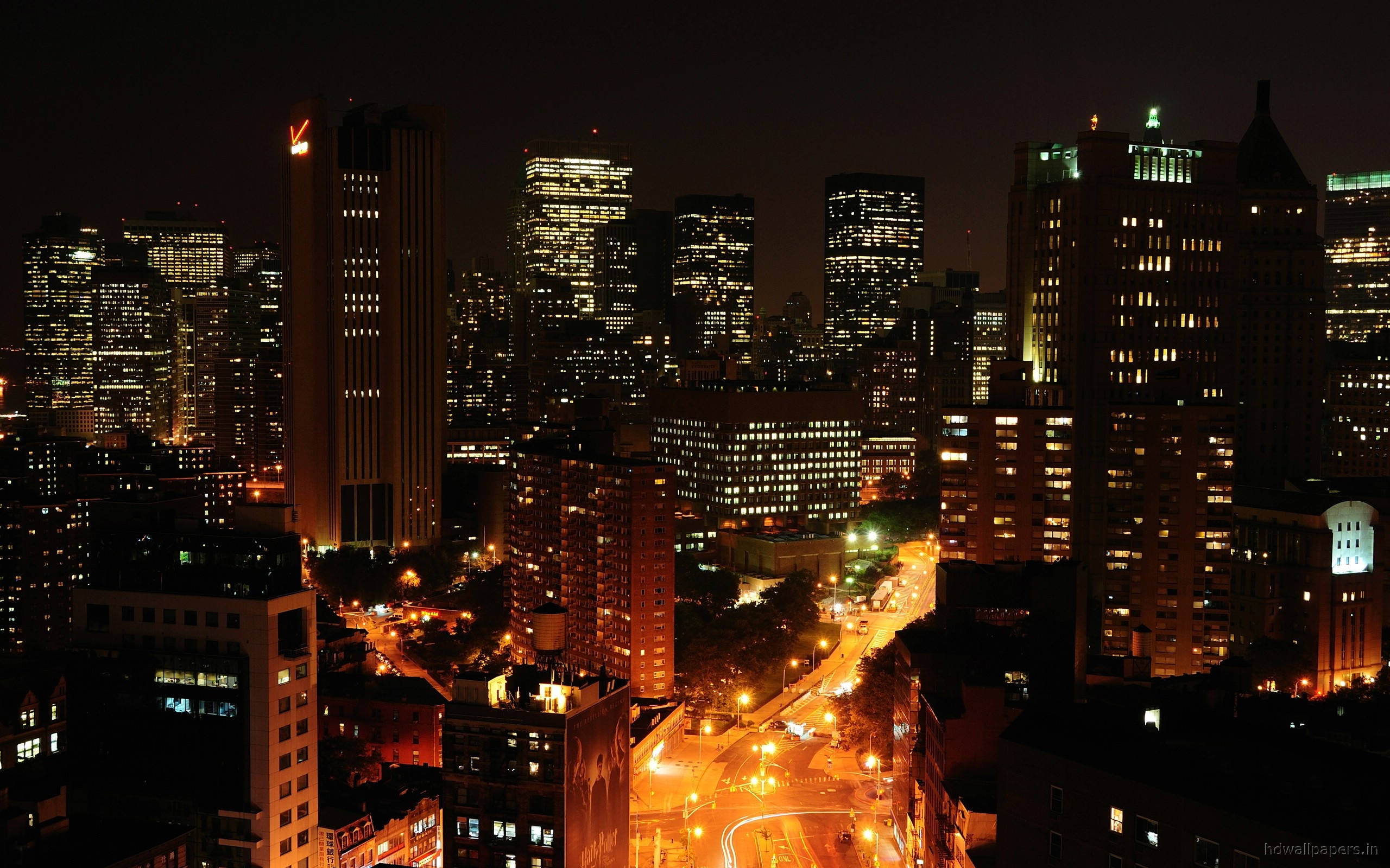 Skyscraper 桌布 壁紙 — 充滿活力的夜景城市景觀，高聳的摩天大樓閃爍著溫暖的光芒，下方蜿蜒的街道被路燈照亮。
