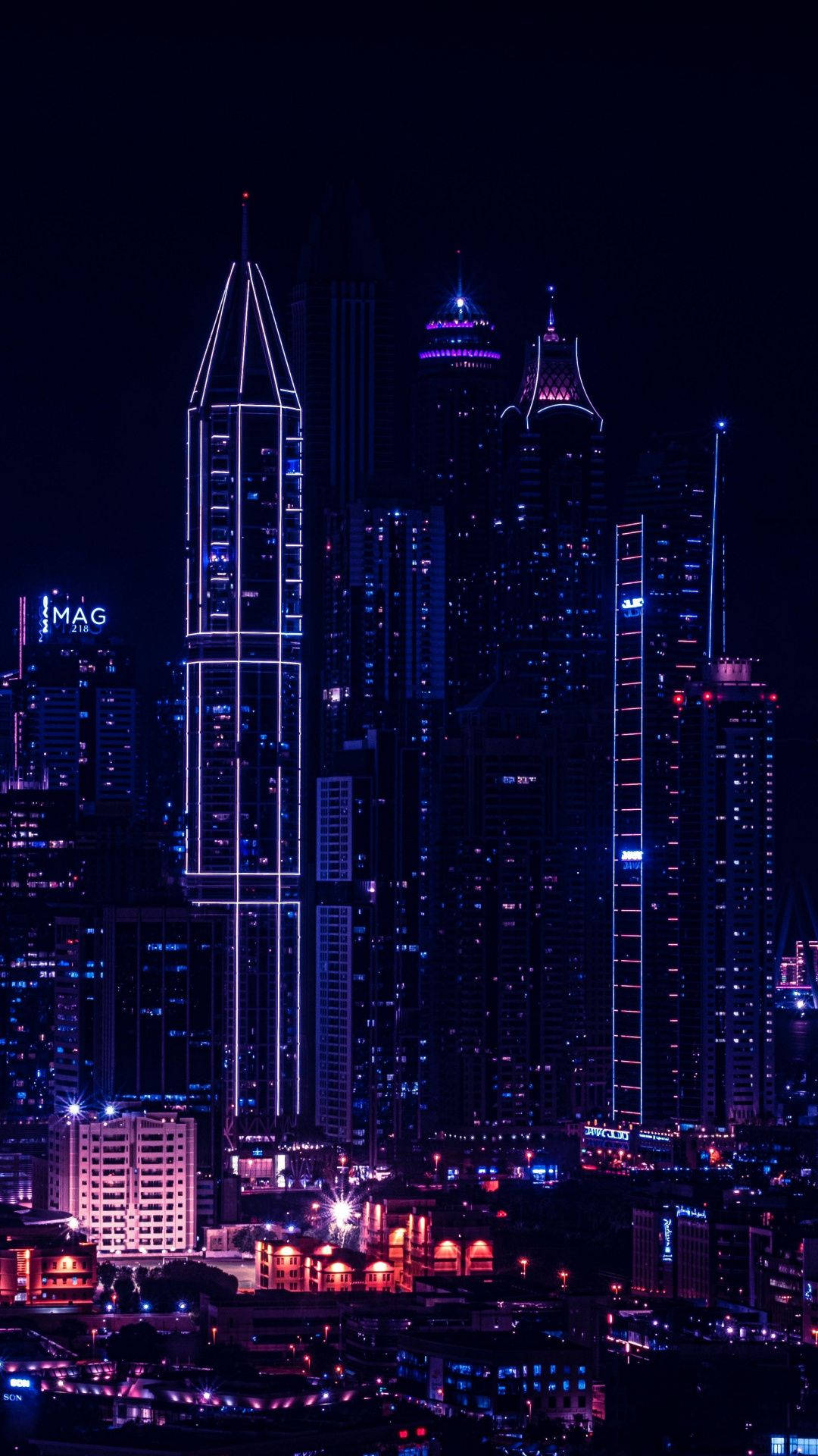 桌布 壁紙 — 充滿活力的夜景城市景觀，高聳的摩天大樓在黑暗的天空中閃爍著電藍色和紫色的霓虹燈光。