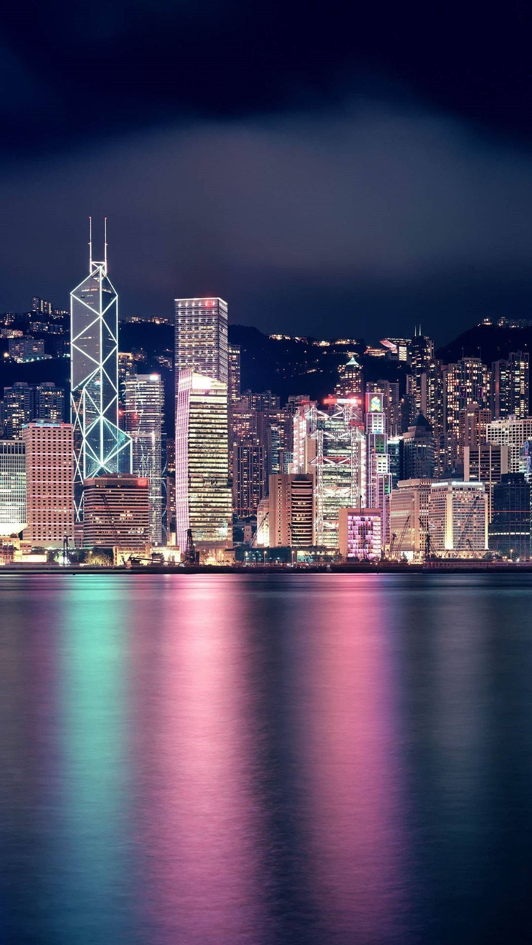 new york city iPhone x 桌布 壁紙 — 充滿活力的夜景城市景觀，高聳的摩天大樓在平靜的水面上反射出五彩繽紛的燈光。