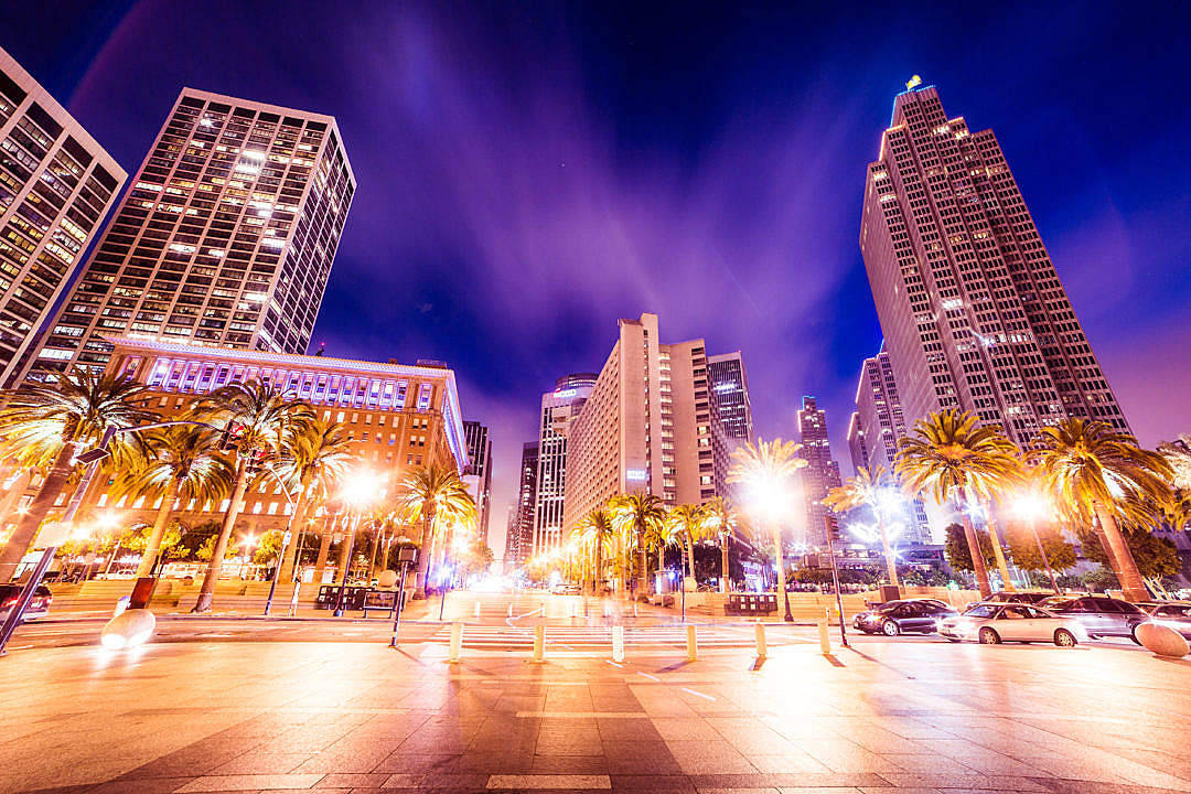 Building 桌布 壁紙 — 充滿活力的夜景城市景觀，高聳的摩天大樓在深紫色天空下閃耀，兩旁種滿棕櫚樹和路燈，投射出溫暖的金色色調。