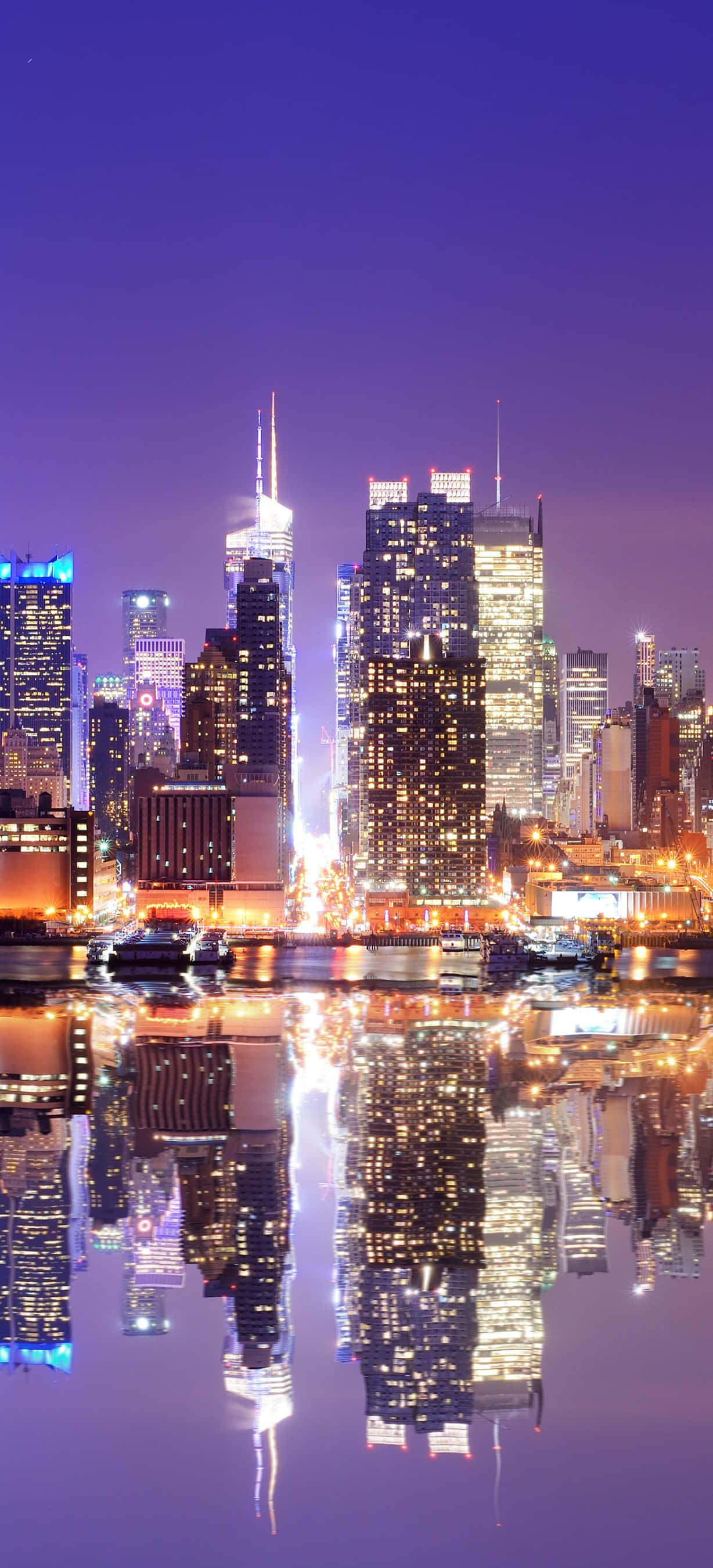 New York 桌布 壁紙 — 充滿活力的夜景城市景觀，高聳的摩天大樓在深紫色天空下閃耀，完美倒映在下方平靜的水面上。