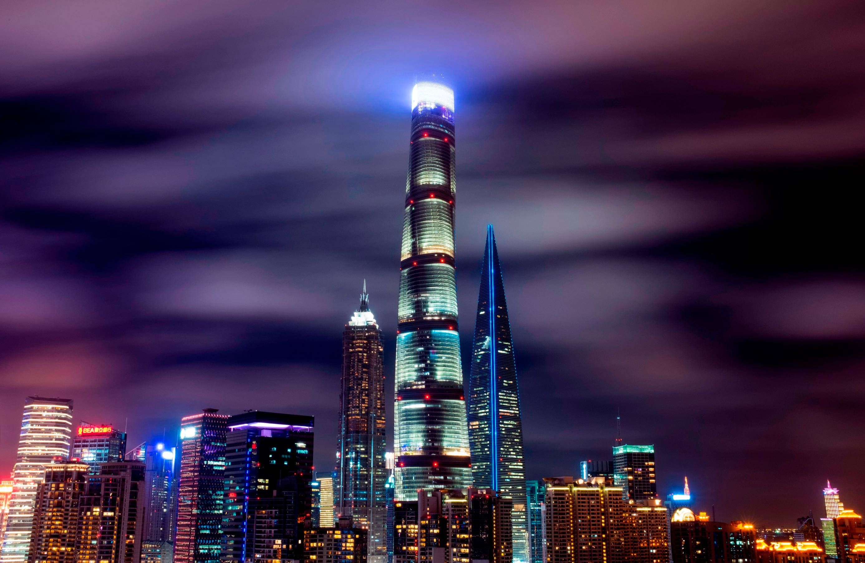 Building 桌布 壁紙 — 充滿活力的夜景城市景觀，高聳的摩天大樓在動態的紫色天空下閃爍著光芒。