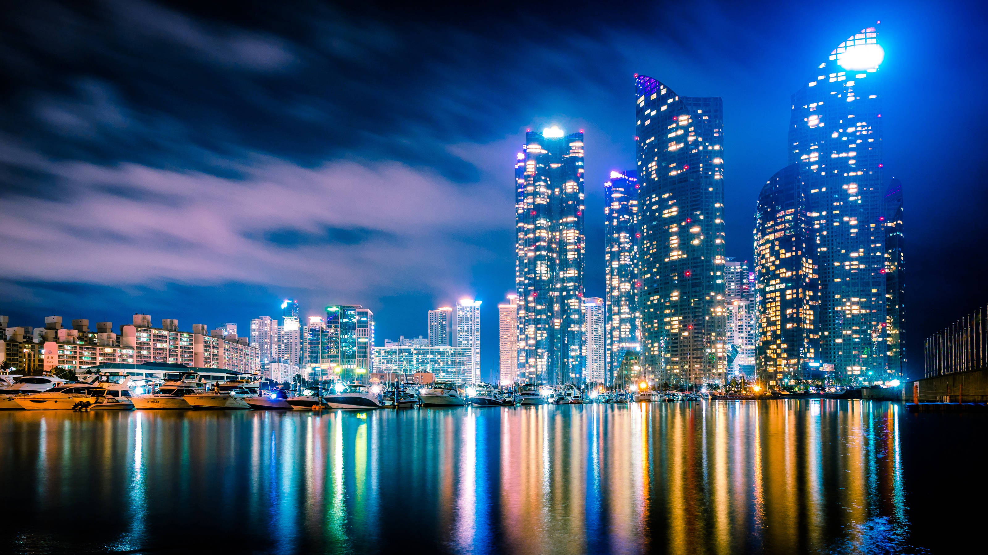 南韓 桌布 壁紙 — 充滿活力的夜景城市景觀，高聳的摩天大樓在平靜的水面上反射出五彩繽紛的燈光。