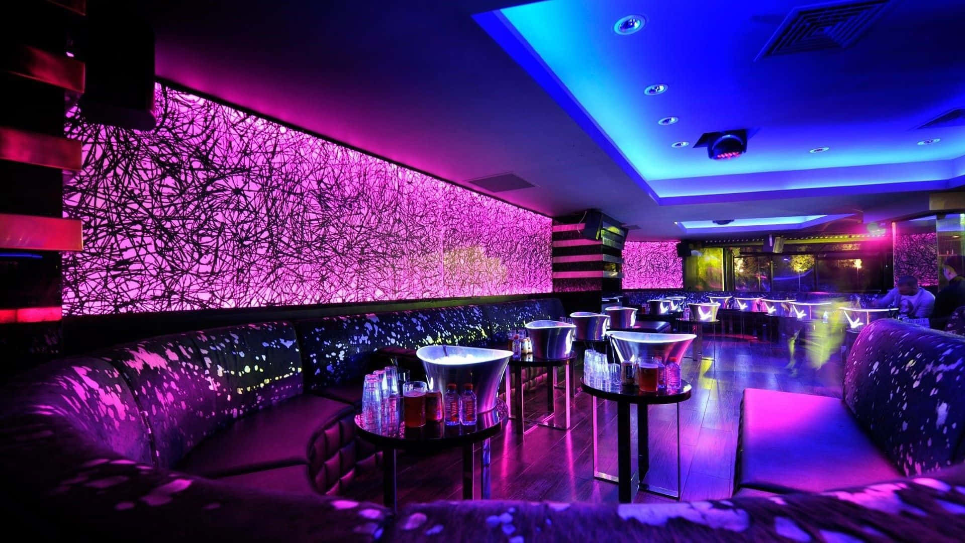 club 桌布 壁紙 — 充滿活力的夜總會，帶有發光的紫色牆壁和藍色天花板燈光，照亮豪華座椅和雞尾酒桌。
